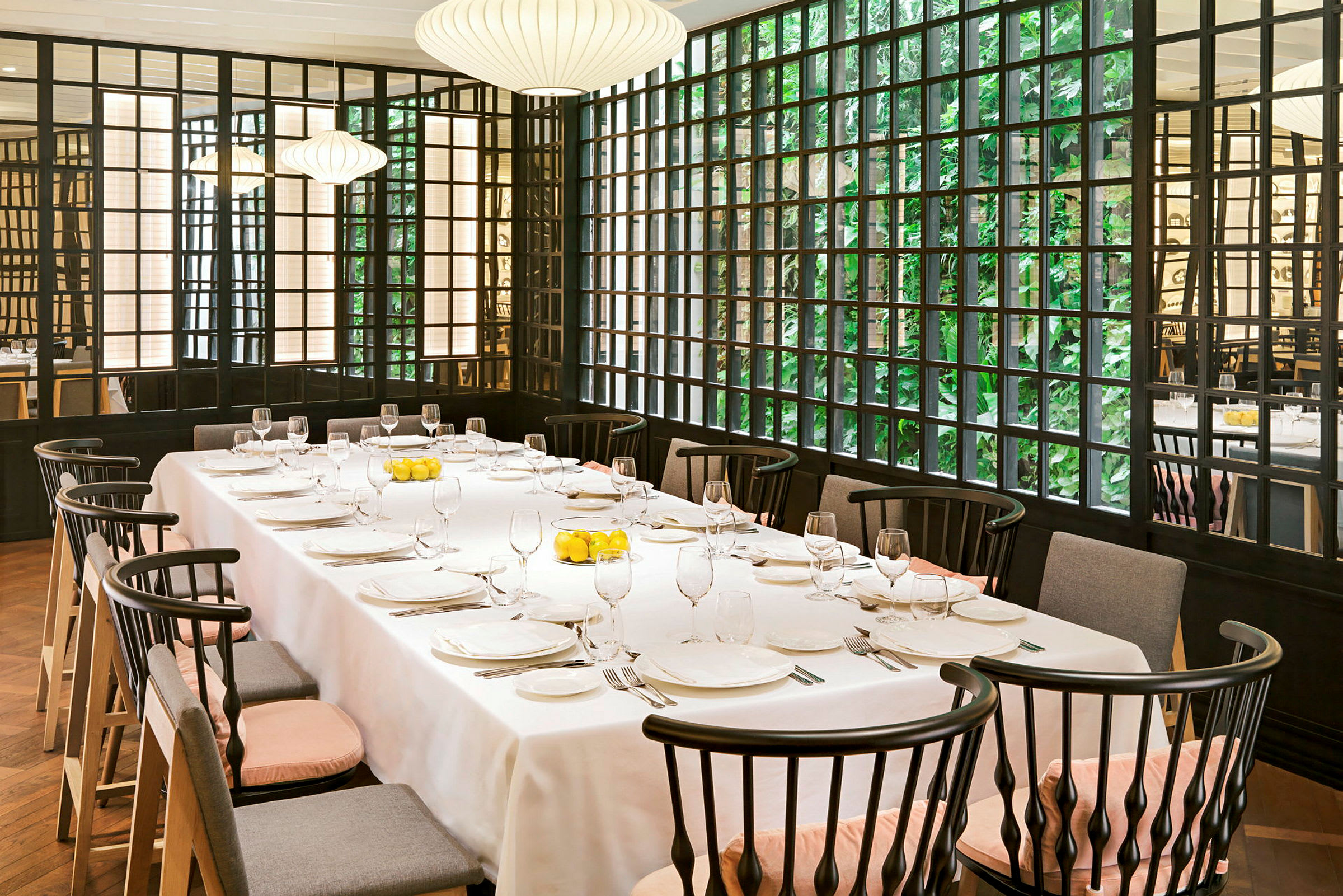Et opdækket bord i en restaurant med elegante stole og store vinduer med grønt udenfor. (AI-genereret tekst)