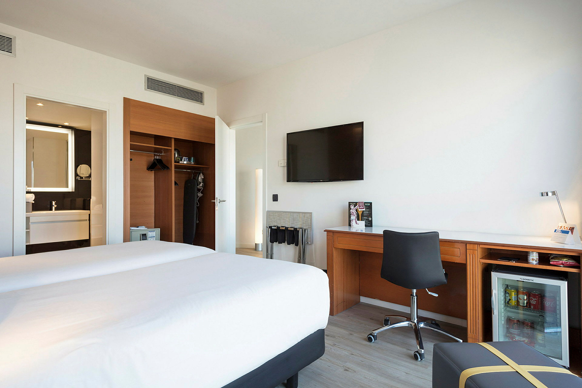 Hotelværelse med to senge, et skrivebord og et skab samt badeværelse i baggrunden. (AI-genereret tekst)