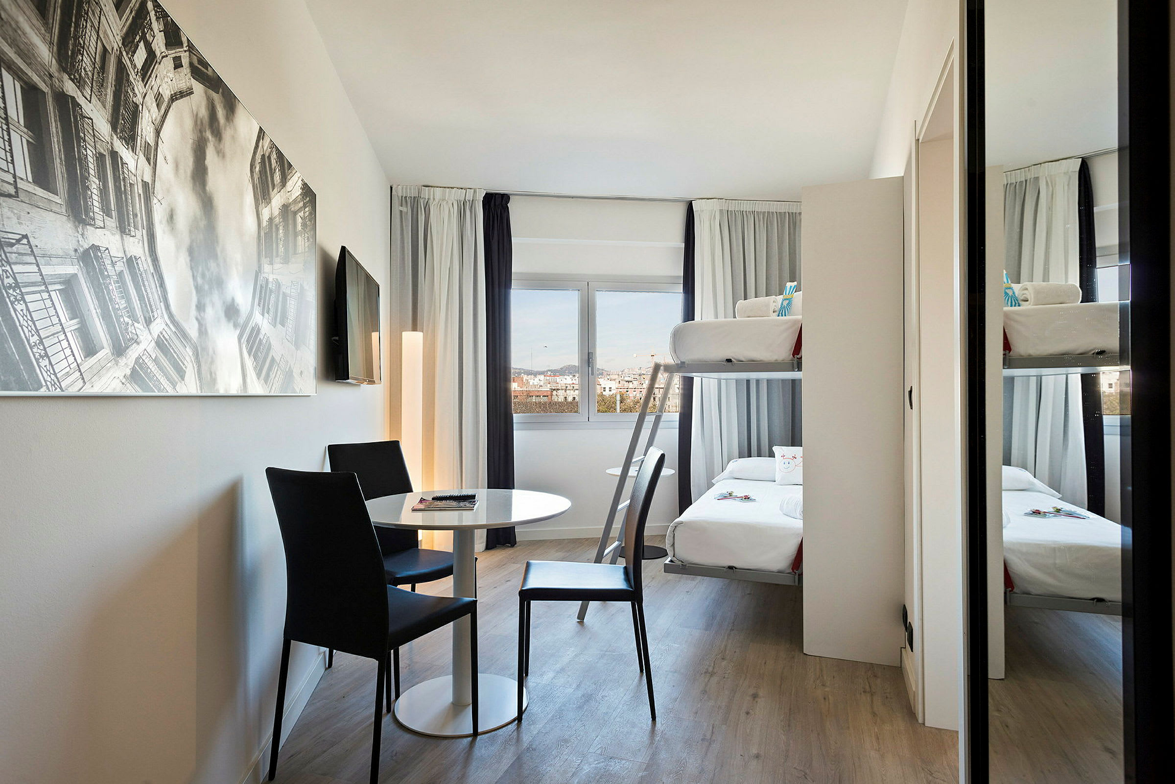 Et moderne hotelværelse med køjeseng, bord og to stole samt et stort vægbillede. (AI-genereret tekst)