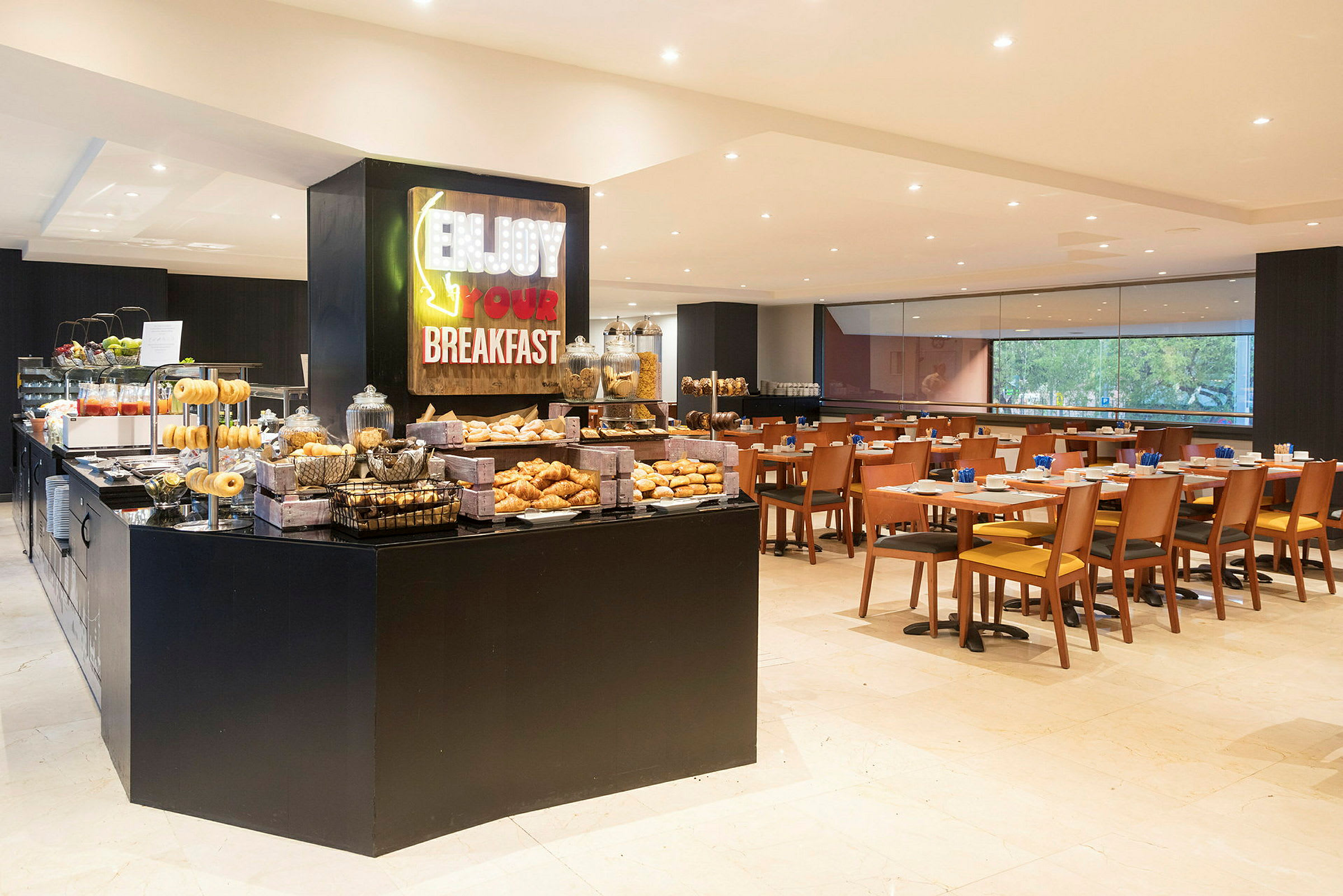 Billede af en morgenmadsbuffet og spiseområde. Buffeten tilbyder et udvalg af bagværk og drikkevarer. (AI-genereret tekst)
