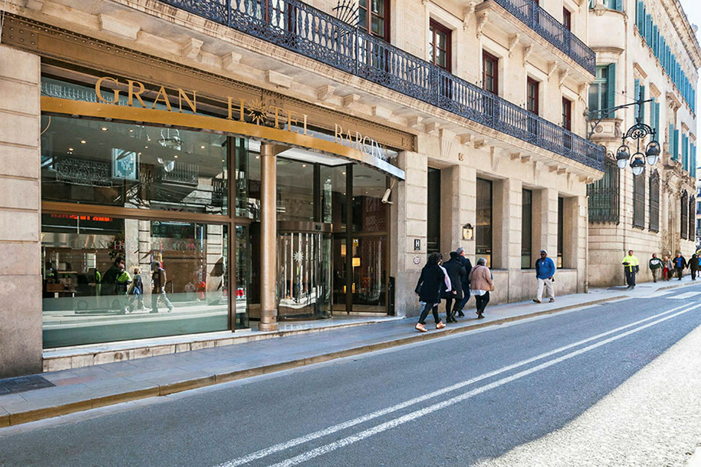En gade med bygninger og indgangen til et hotel med skiltet "Gran Hotel Barcino". (AI-genereret tekst)