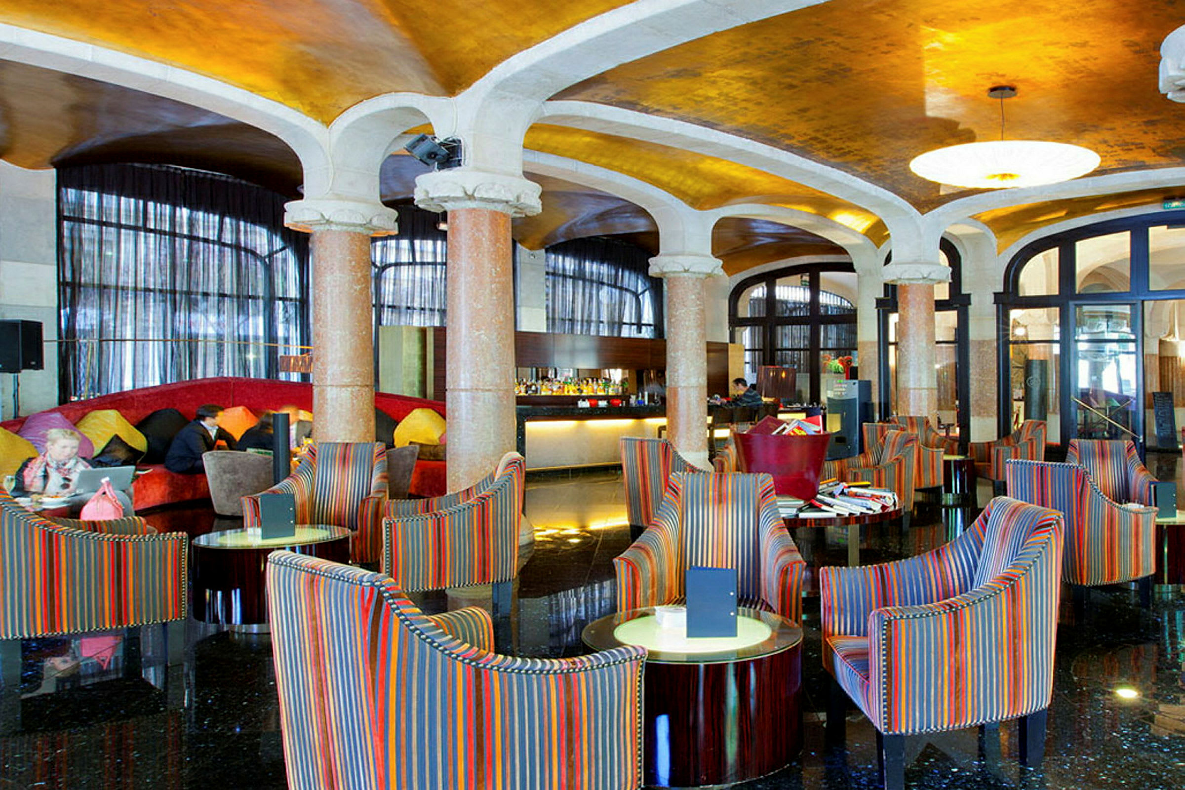 Et elegant hotellobbyområde med farverige lænestole og runde borde, marmorsøjler og et skinnende gulv. (AI-genereret tekst)