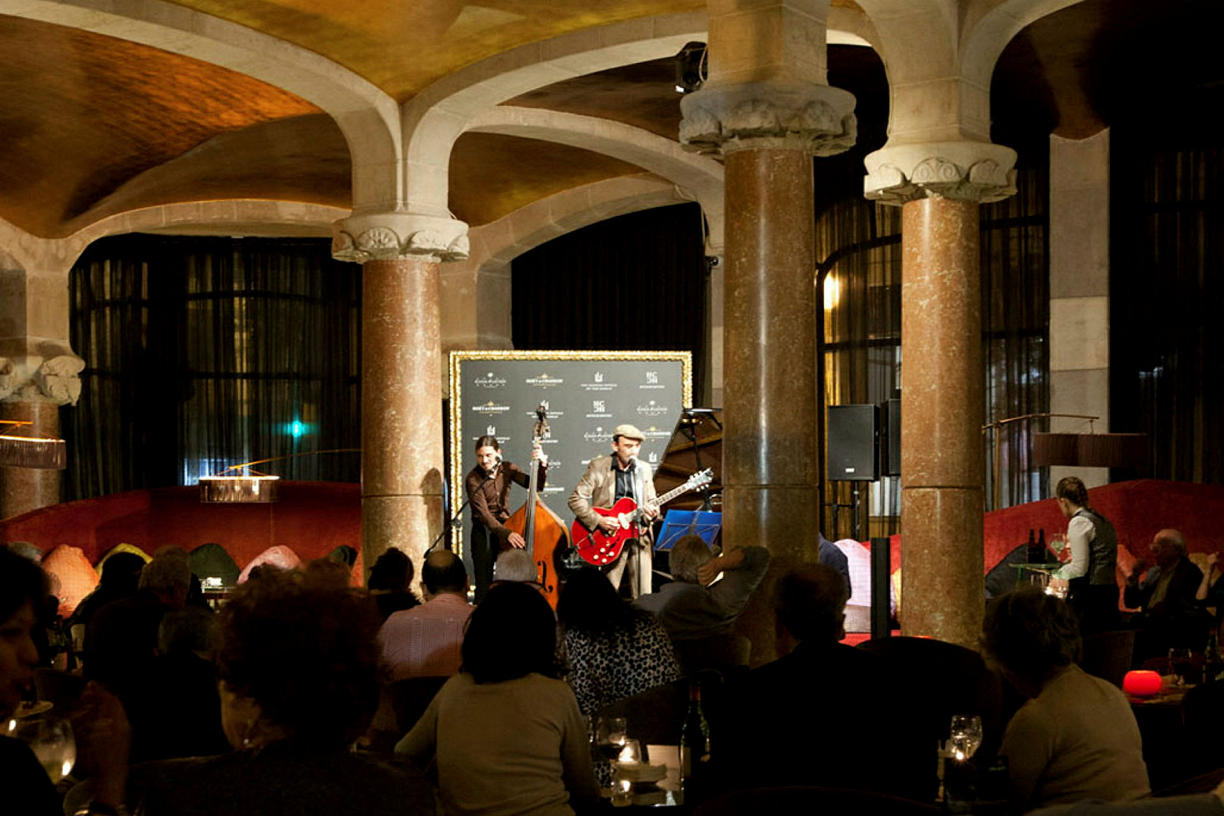 En indendørsscene, hvor musikere optræder foran et siddende publikum i en elegant atmosfære. (AI-genereret tekst)