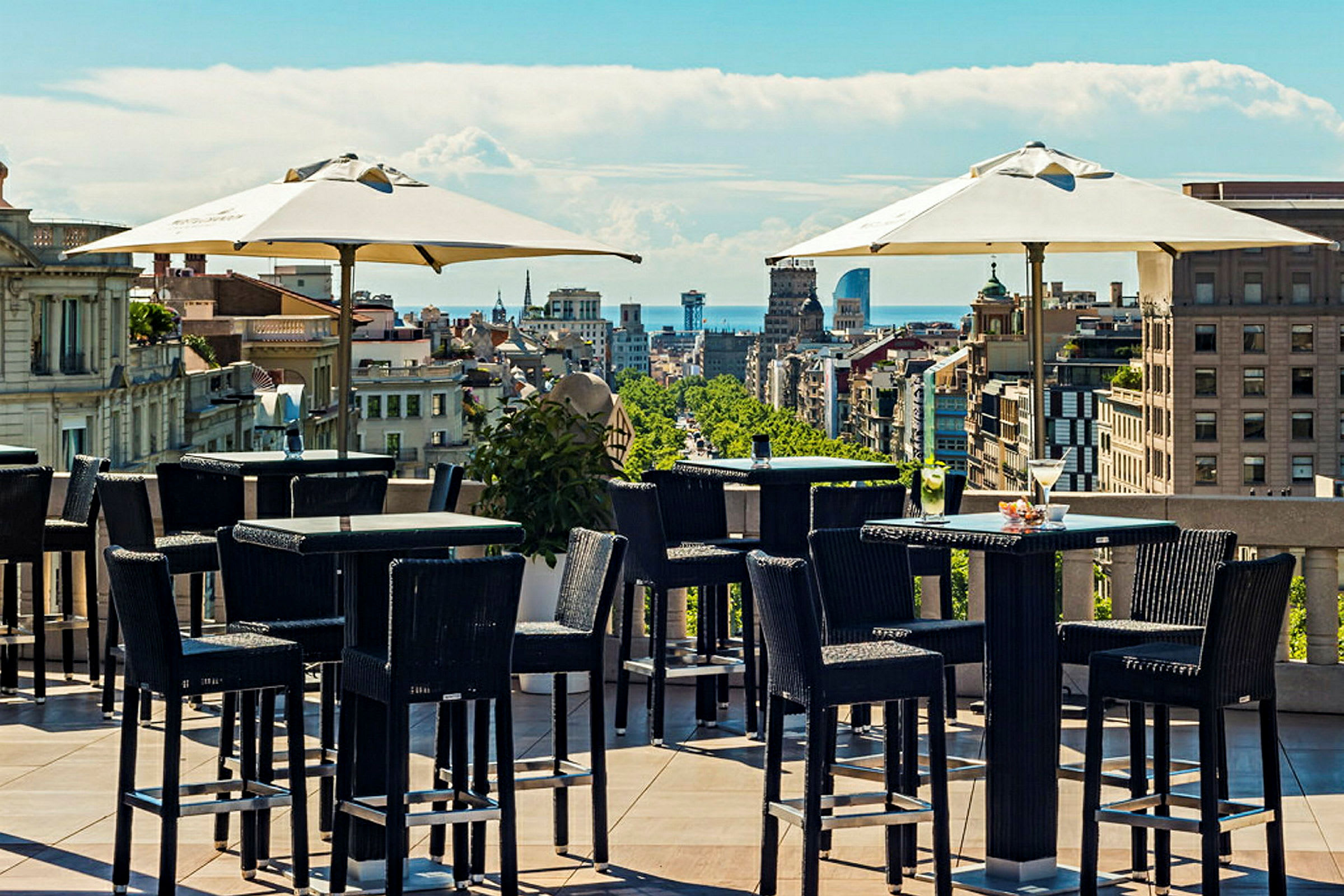 Udendørs servering på en tagterrasse med udendørsmøbler og udsigt over byens silhuet under en klar blå himmel. (AI-genereret tekst)