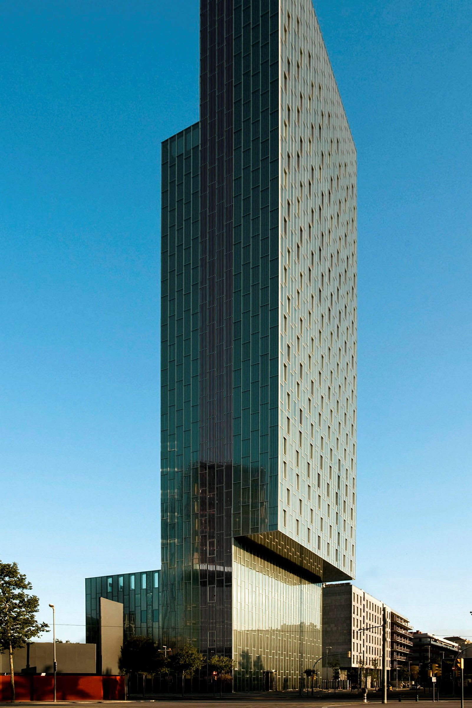 Høj bygning med moderne arkitektur omgivet af blå himmel og urbane bygninger. (AI-genereret tekst)