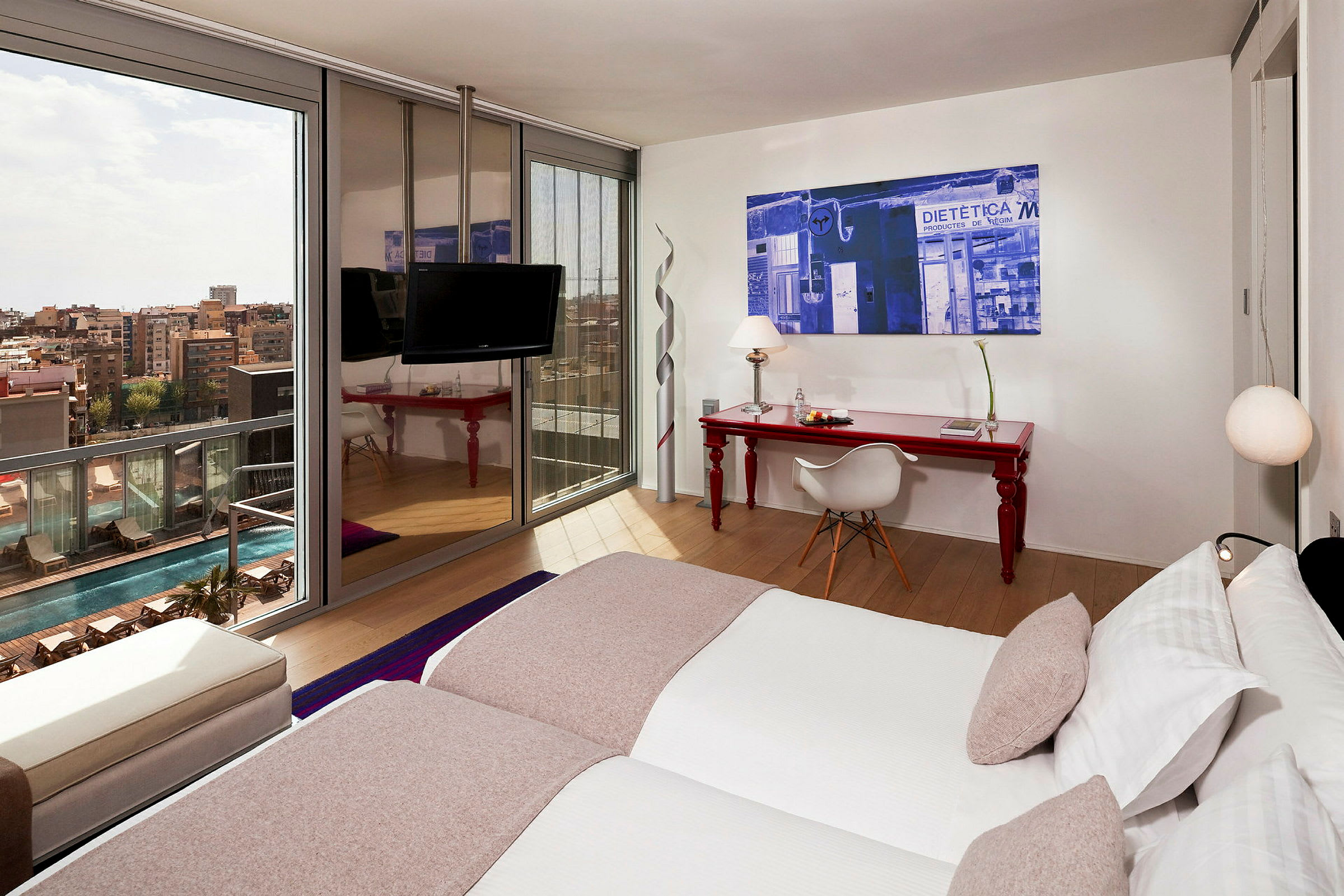 Et moderne hotelværelse med to enkeltsenge, et rødt skrivebord med stol og et stort vindue, der vender mod poolområdet og byen. (AI-genereret tekst)