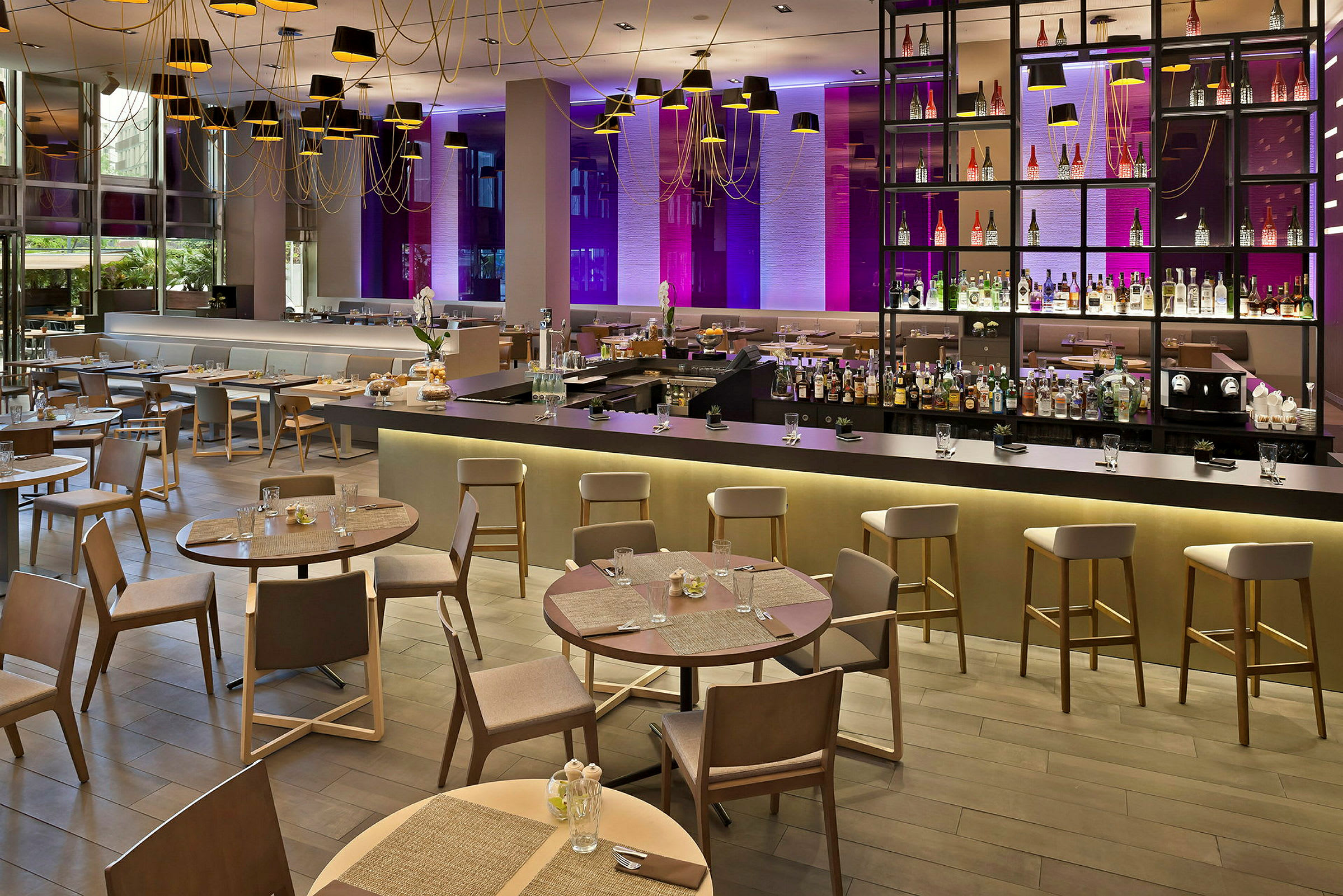Billede af en moderne restaurant med elegante borde og stole, en lang bardisk og en dekorativ bagvæg med flasker samt belysning. (AI-genereret tekst)