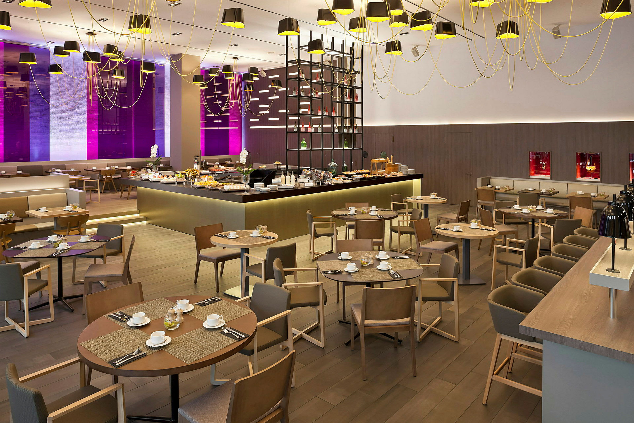 En restaurantinteriør med spiseborde og stole samt et madserveringsområde omgivet af moderne belysning og indretning. (AI-genereret tekst)