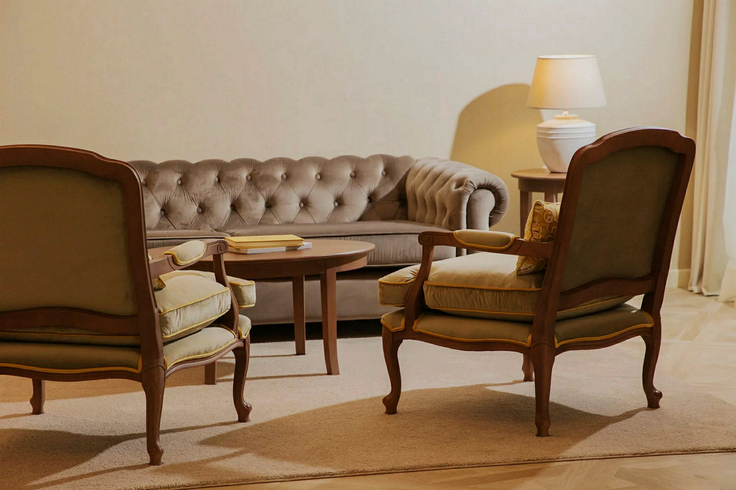 En siddegruppe med en beige sofa, to lænestole og et sofabord. En lampe på et sidebord ses i baggrunden. (AI-genereret tekst)