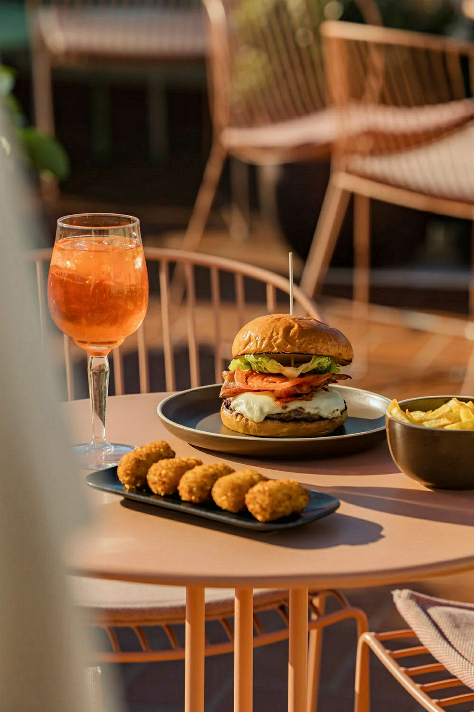 En tallerken med burger og pommes frites, ved siden af et fad med små snacks og et glas orange drikke. (AI-genereret tekst)