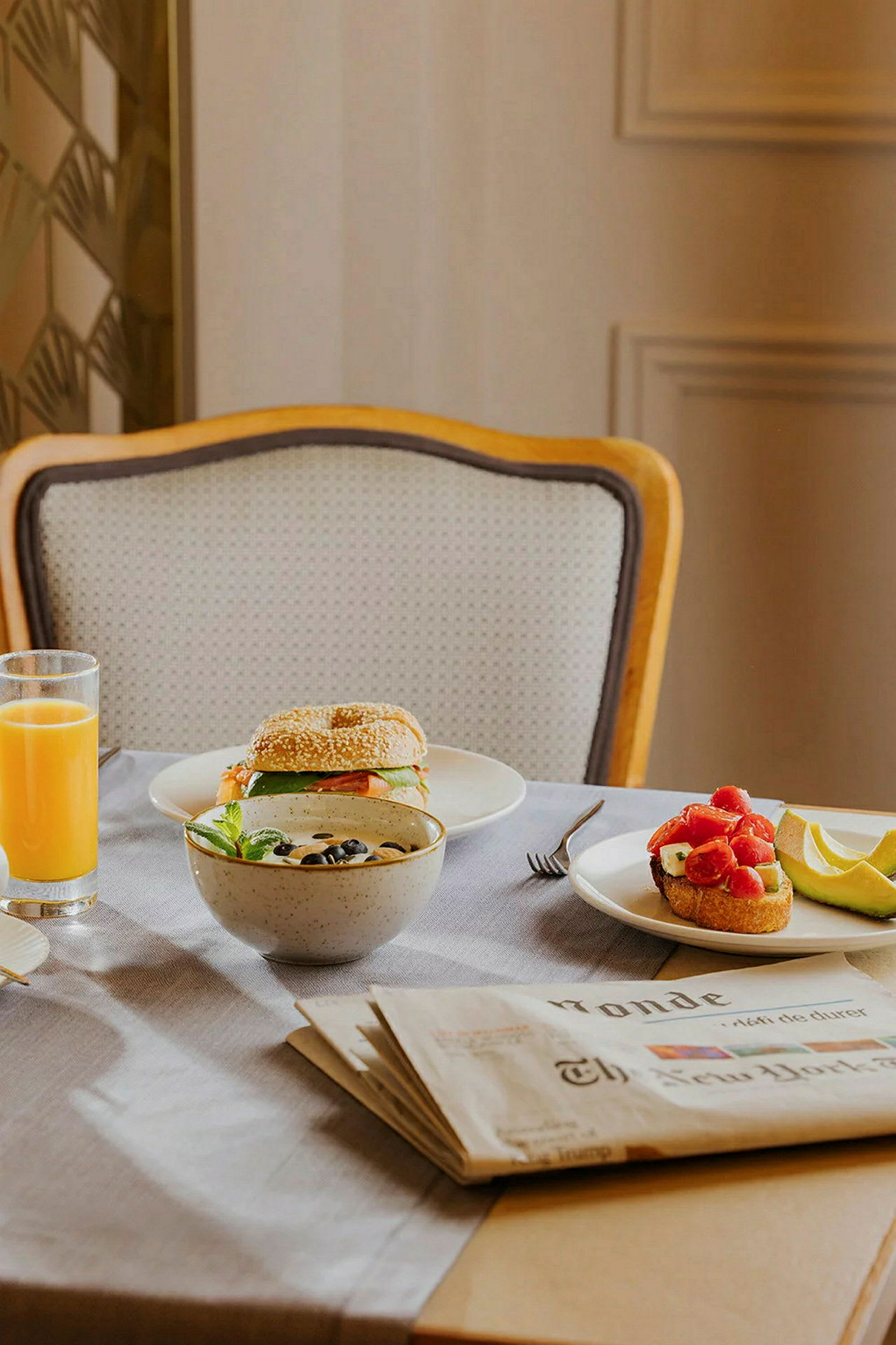 Et dækket bord med sandwich, en skål skyr med oliven, et glas juice og en avis. (AI-genereret tekst)