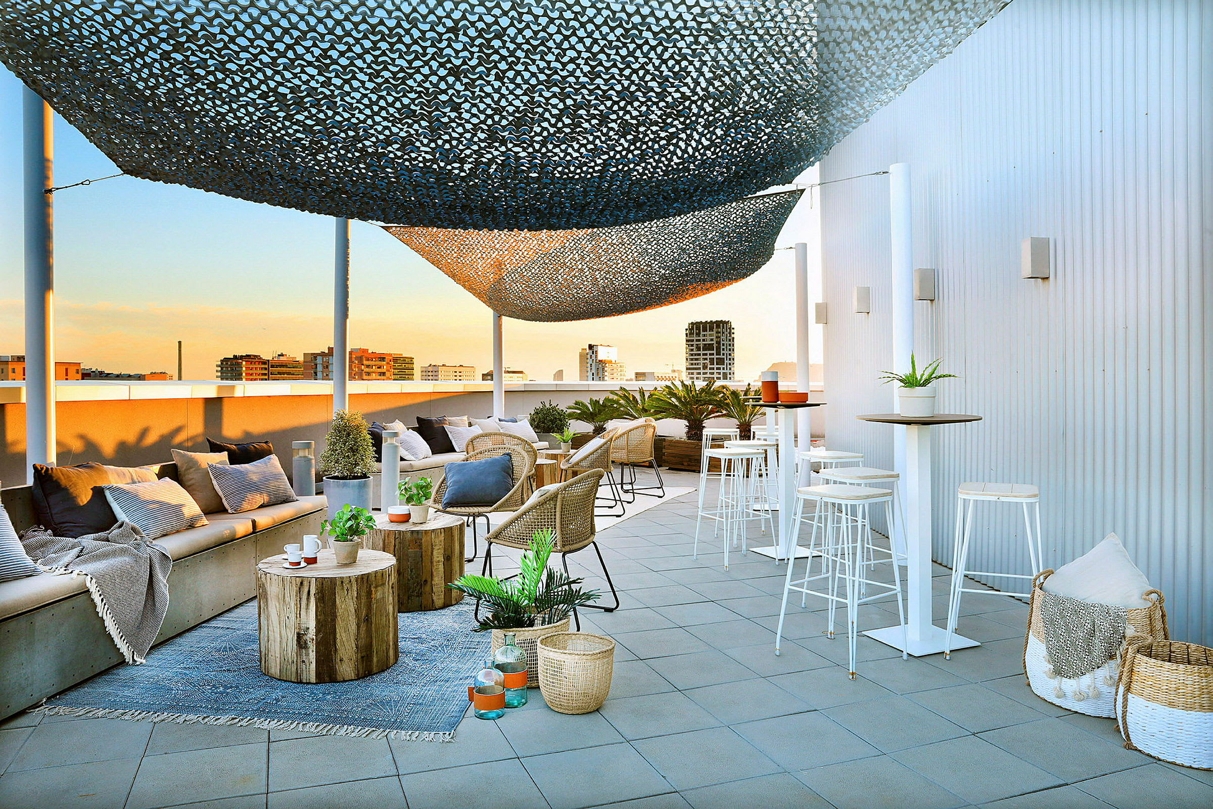 En moderne tagterrasse med siddepladser, borde og dekorationer. Et solsejl hænger over, og byen kan ses i baggrunden. (AI-genereret tekst)