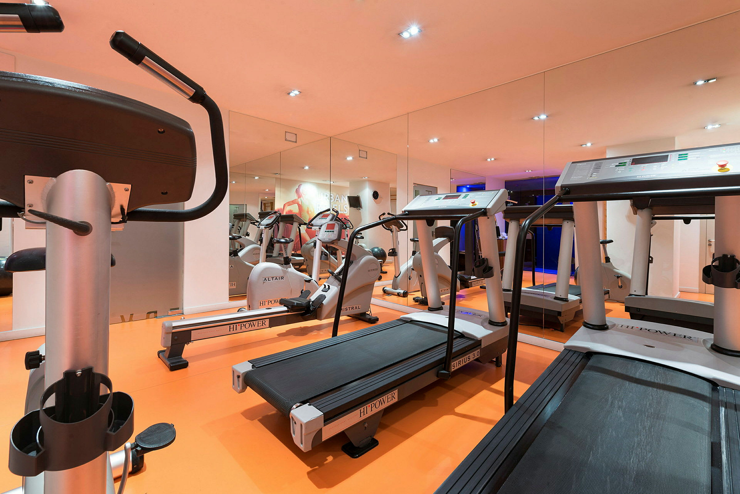 Et fitnesscenter med træningsmaskiner, herunder løbebånd og motionscykler. Væggene har spejle. (AI-genereret tekst)