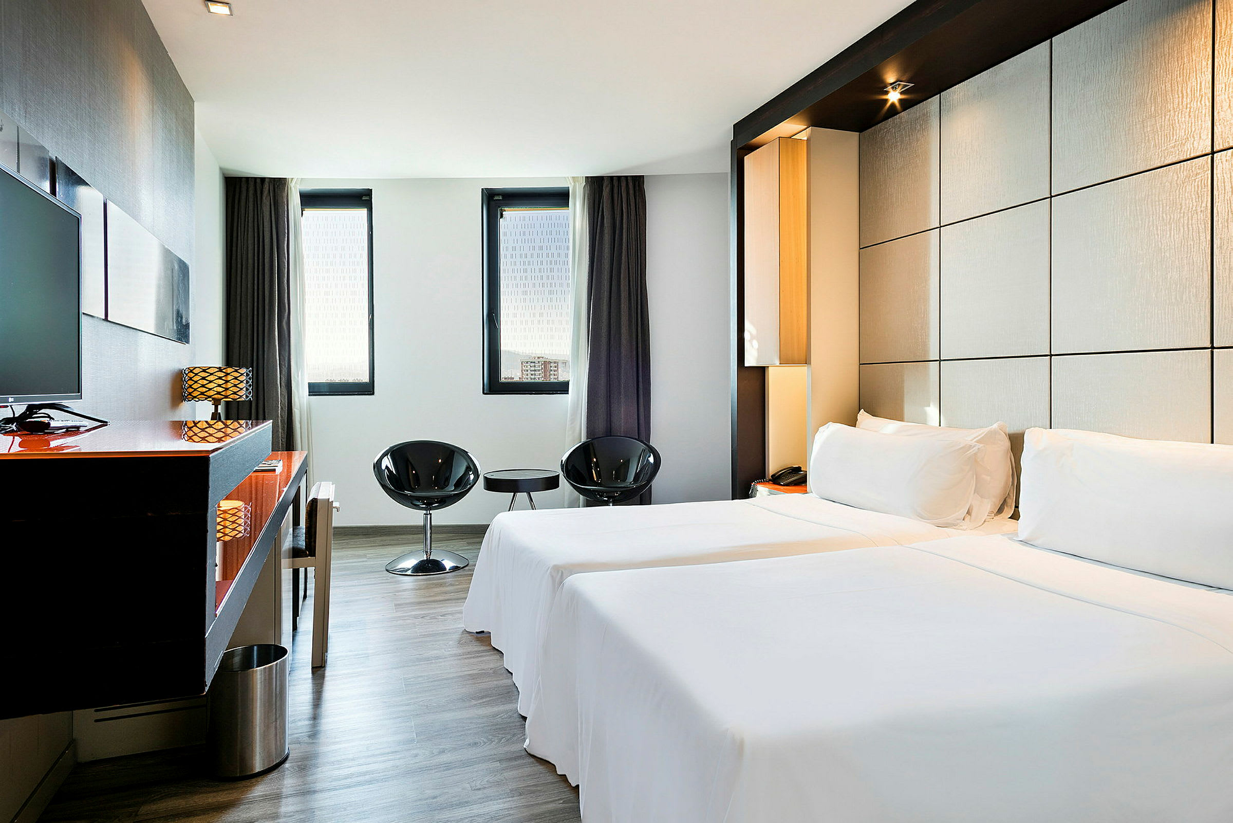Et elegant hotelværelse med to enkeltsenge, minimalistisk indretning og store vinduer, der lader naturligt lys komme ind. (AI-genereret tekst)