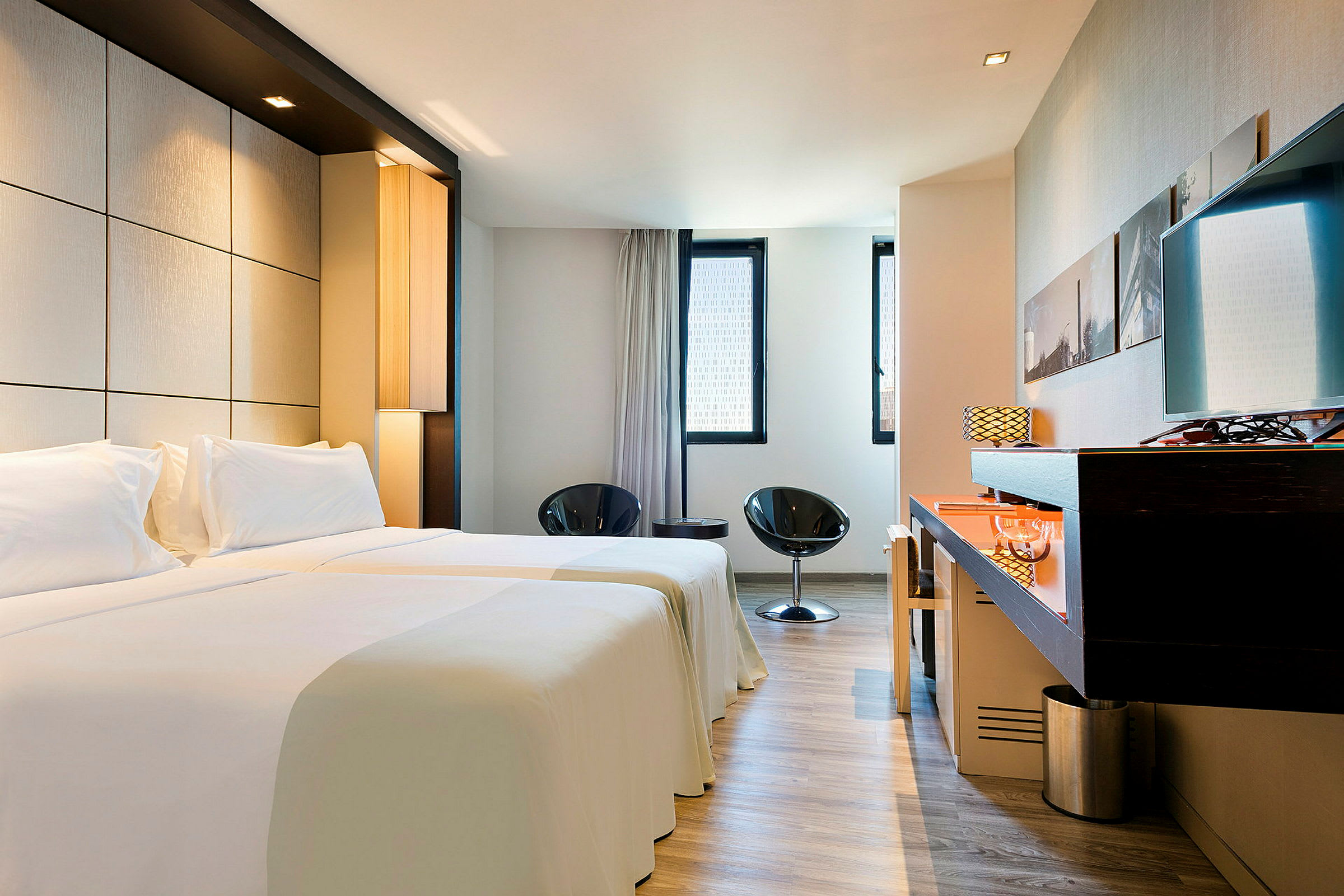 Et moderne hotelværelse med to enkeltsenge, lille siddeområde og skrivebord. (AI-genereret tekst)