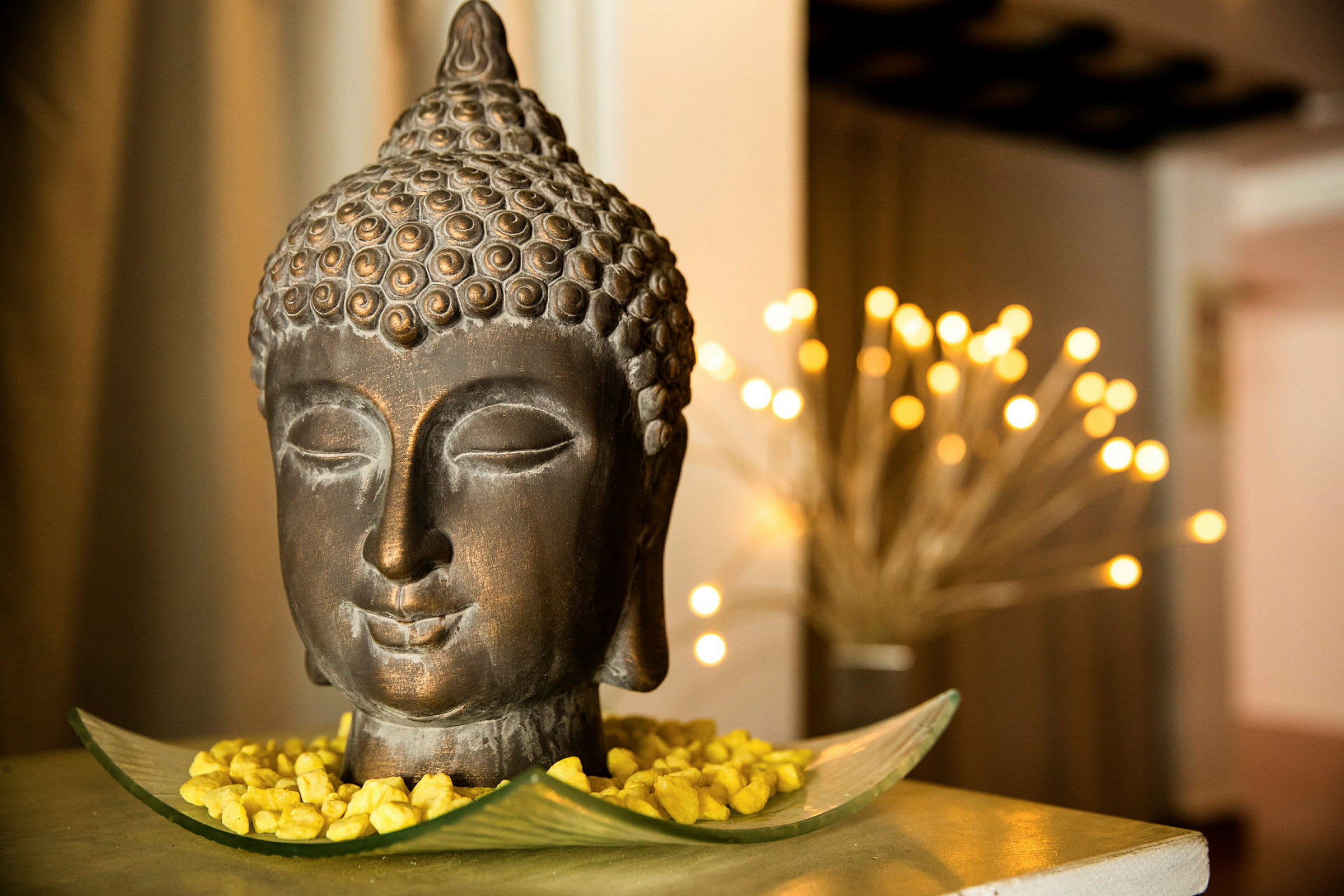 En dekorativ Buddha-figur placeret på en skål med guldfarvede sten. Blødt lys i baggrunden. (AI-genereret tekst)