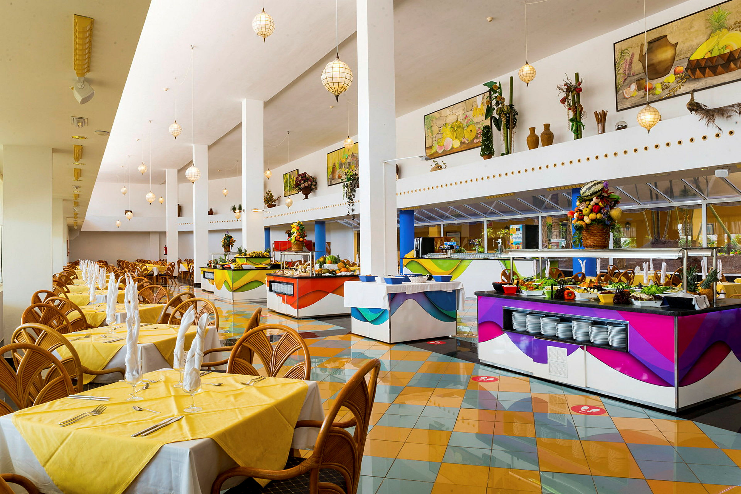 En rummelig restaurant med luftige lokaler, gule duge på bordene og flere farverige buffetstationer. (AI-genereret tekst)