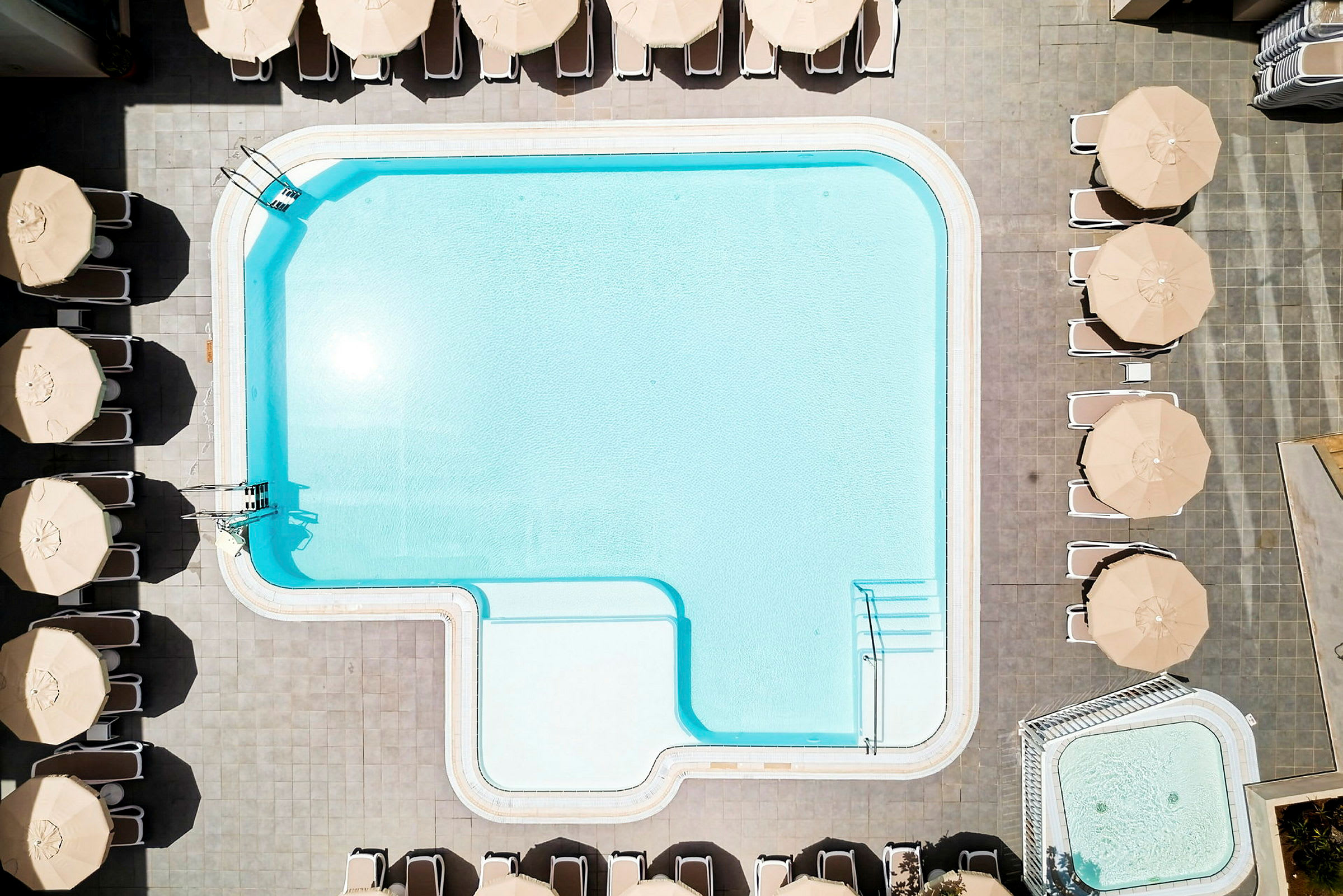 En udendørs pool med omkringliggende parasoller og liggestole. (AI-genereret tekst)