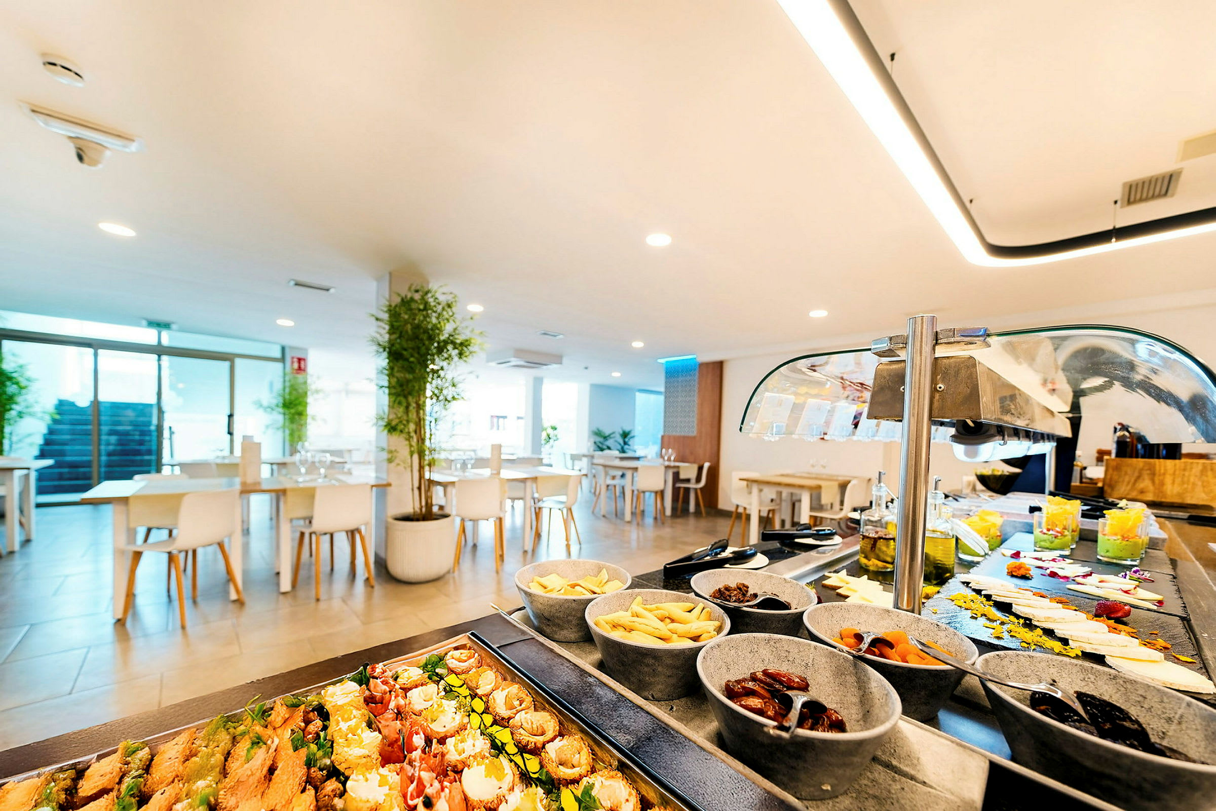 En lys restaurationsinteriør med buffetbord fyldt med forskellige retter og små skåle. (AI-genereret tekst)