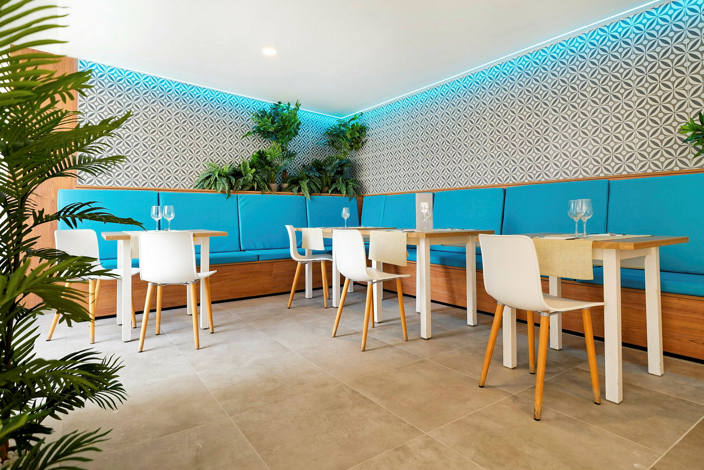 En moderne restaurant med lyse møbler, turkise sædehynder og planter som dekoration langs væggene. (AI-genereret tekst)