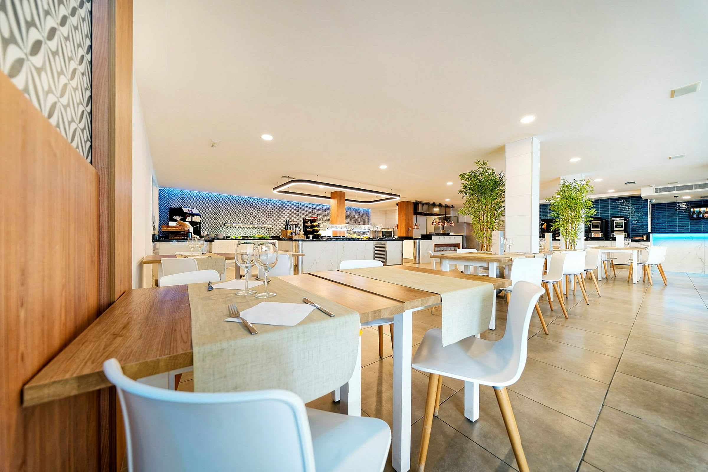 Et moderne restaurantområde med træborde og hvide stole, dekoreret med planter og blød belysning. (AI-genereret tekst)