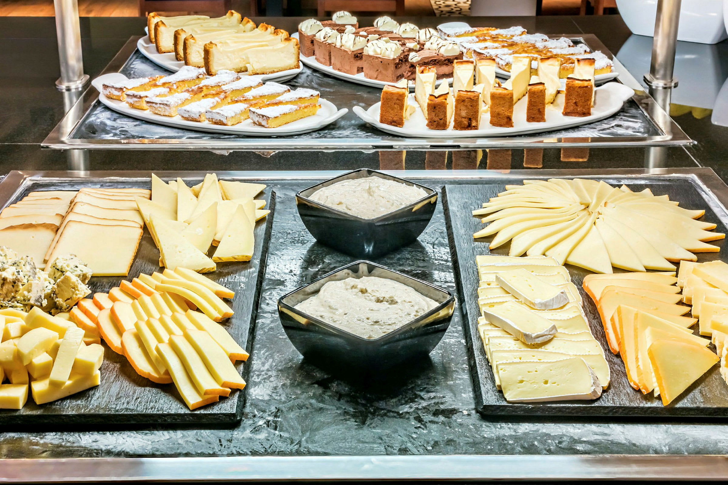 Billede af en buffet med forskellige typer ost, dip i skåle og bagværk på fade. (AI-genereret tekst)