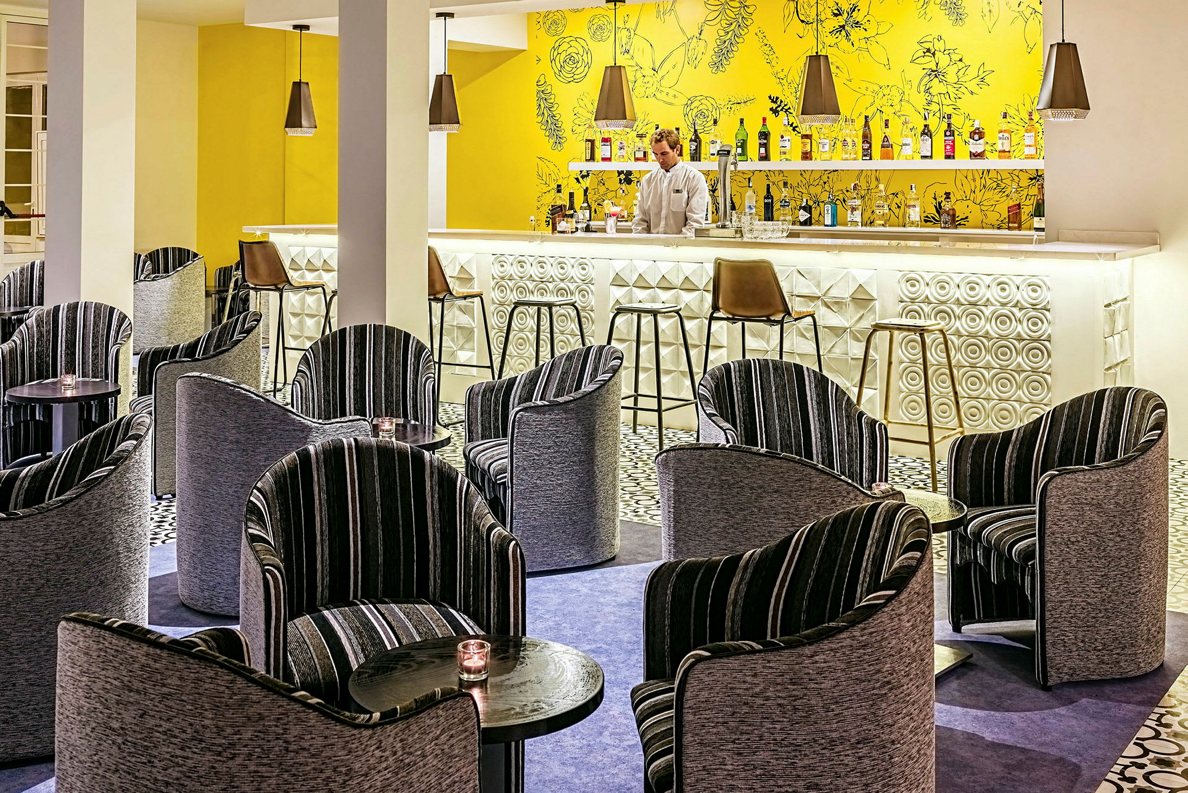 En hotelbar med farverigt interiør, herunder moderne stole og små borde. (AI-genereret tekst)