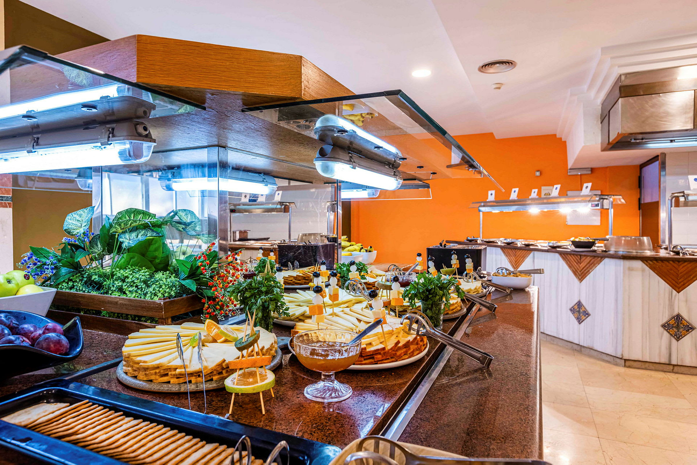 En buffet med forskellige madvarer, herunder ost, kiks og frugt, samt dekorative planter. (AI-genereret tekst)