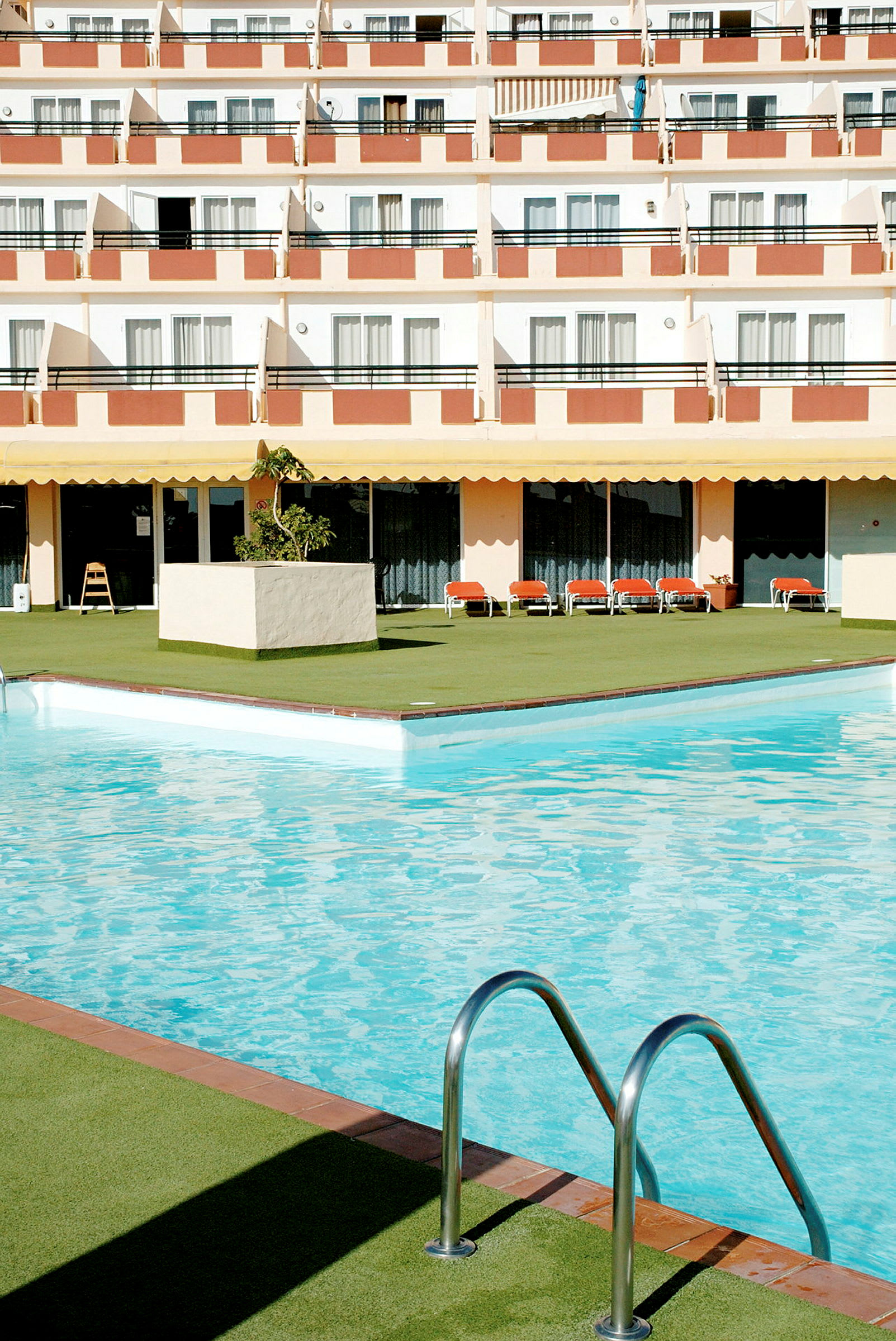 Billede af en hotelpool med liggestole og altaner i baggrunden. (AI-genereret tekst)