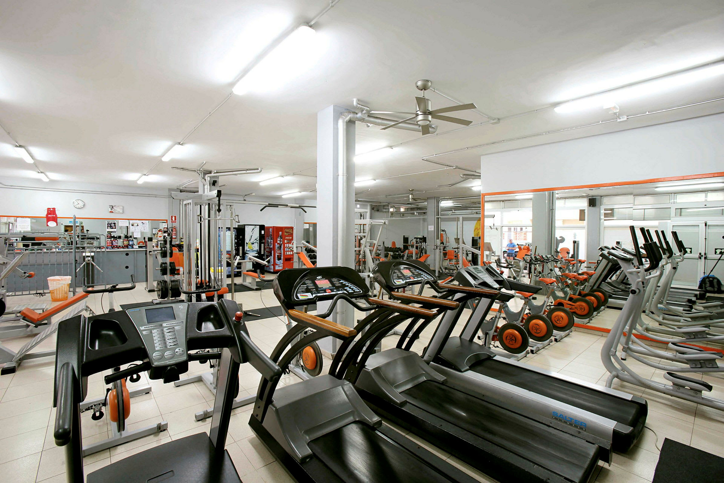 Et fitnesscenter med forskellige træningsmaskiner og udstyr som løbebånd og cykler. (AI-genereret tekst)