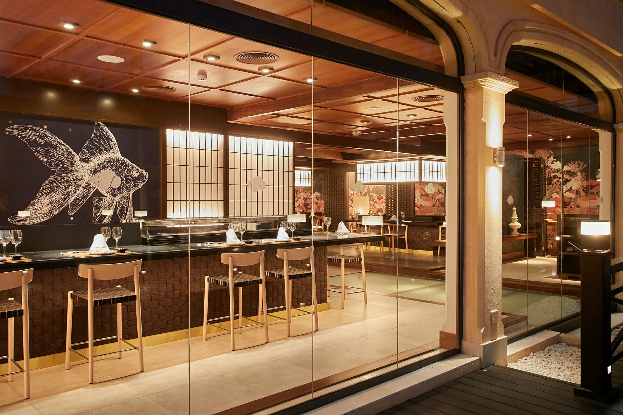 En elegant restaurant med en bar og siddepladser. Der er en stor vægdekoration med et fiskemotiv og belysning, som skaber en varm atmosfære. (AI-genereret tekst)