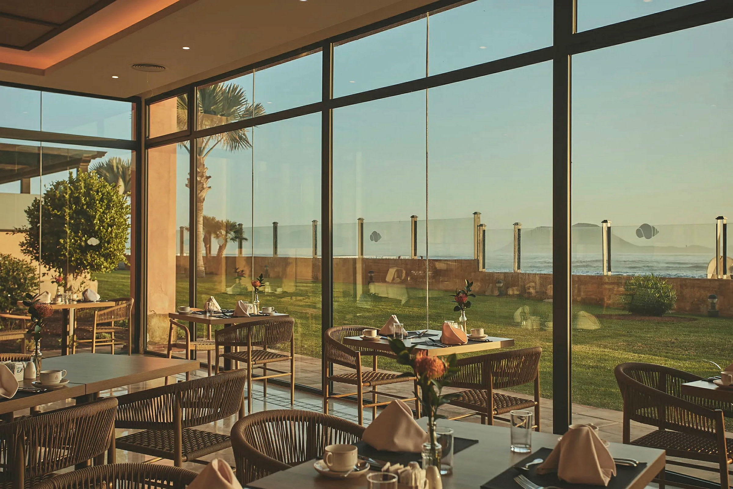 Restaurant med dækkede borde og store vinduer med udsigt til havet. (AI-genereret tekst)