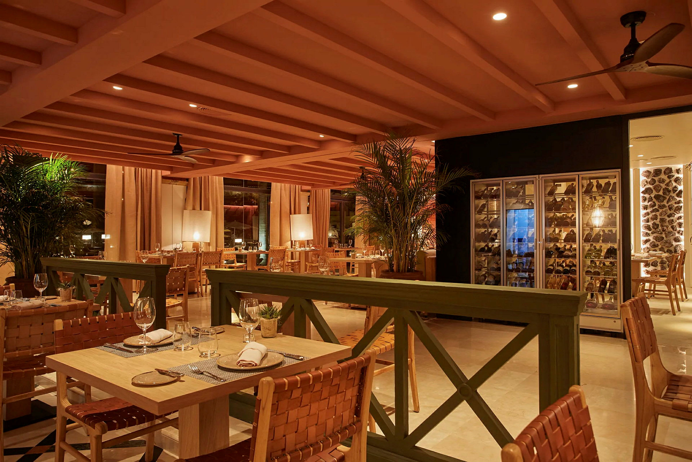 Billede af en elegant restaurant med borde og stole, vinopbevaringsskab til højre og varm belysning. (AI-genereret tekst)