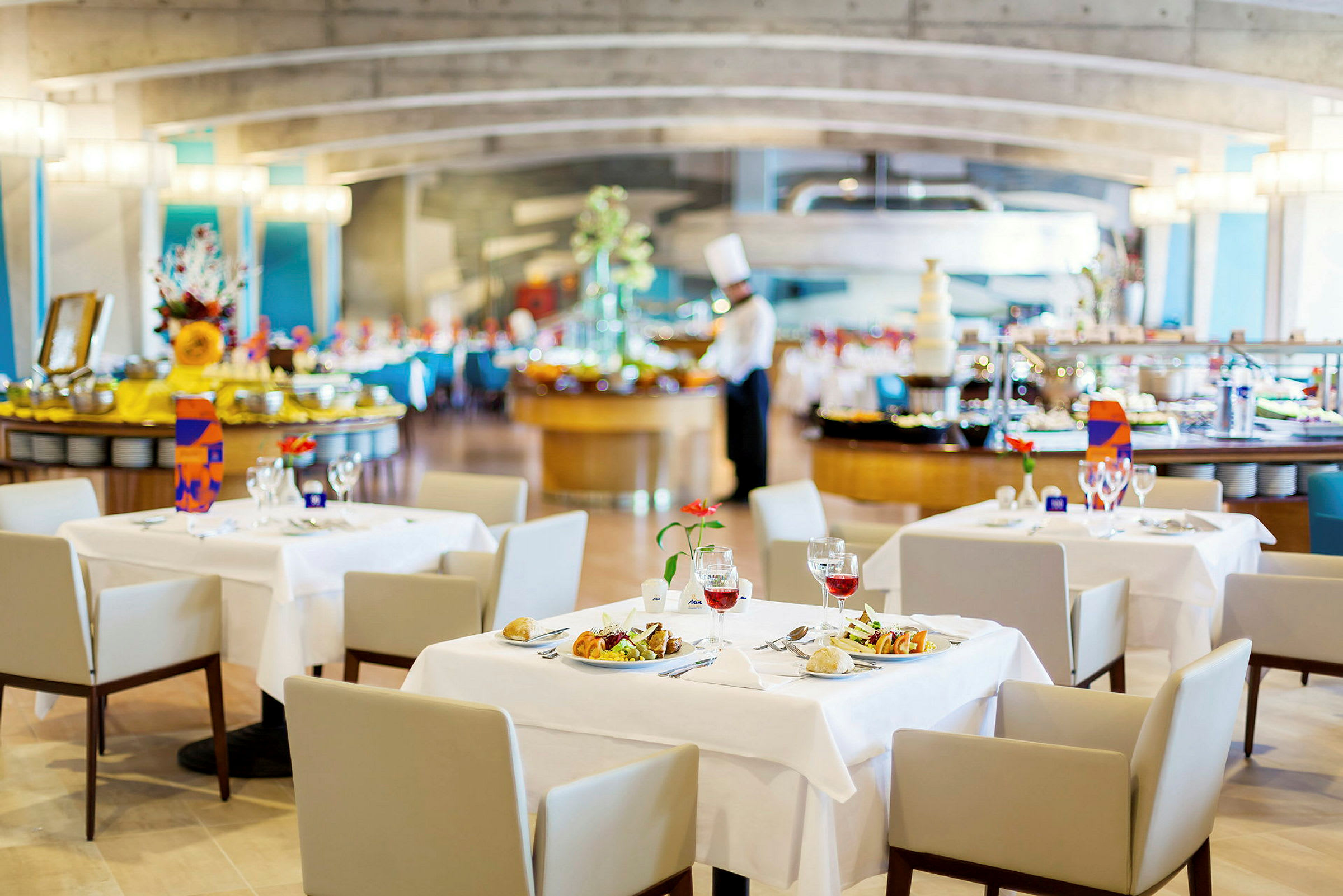 Restaurant med dækkede borde, serveringsområde og en kok i baggrunden. (AI-genereret tekst)