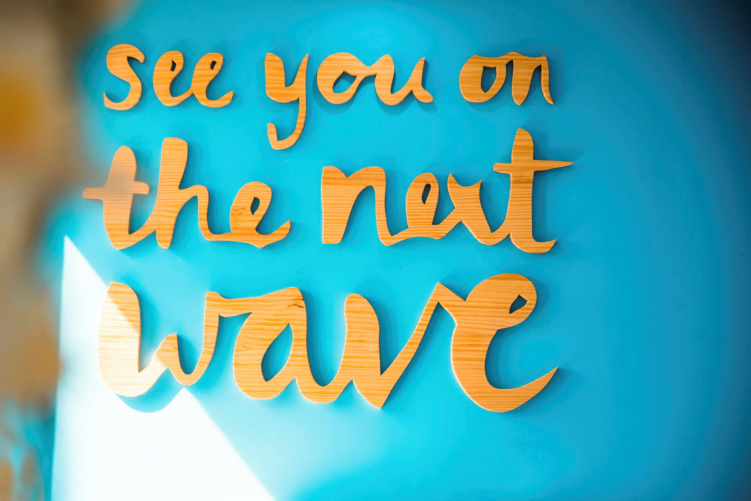 Tekst i træmateriale: "See you on the next wave" på en blå væg. (AI-genereret tekst)