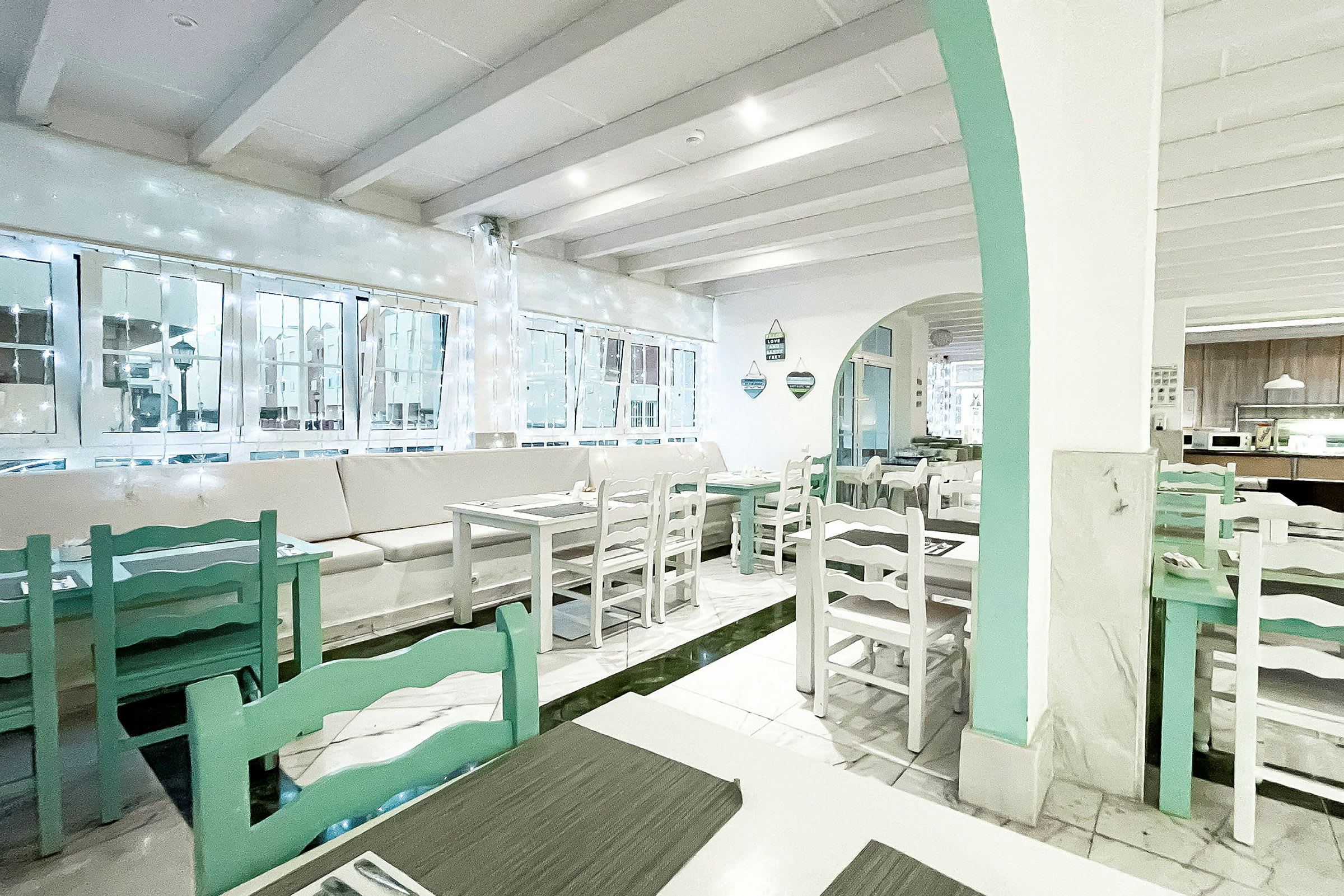 En lys og luftig café eller restaurant med hvide vægge og lysegrønne møbler. (AI-genereret tekst)