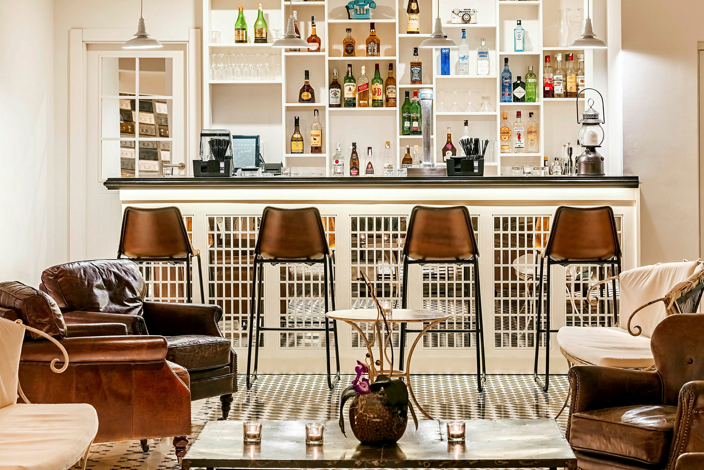 Billede af en elegant bar med brune barstole og komfortable læderstole. Hylderne bag disken er fyldt med flasker og glas. (AI-genereret tekst)