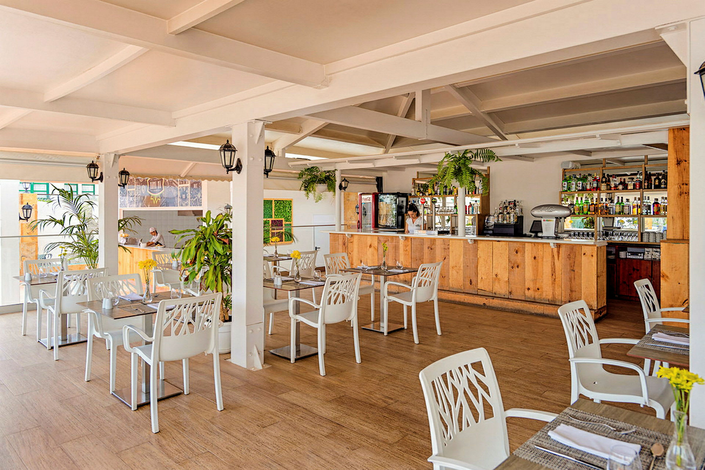 En lys restaurant med hvide borde og stole samt en bardisk i træ. (AI-genereret tekst)