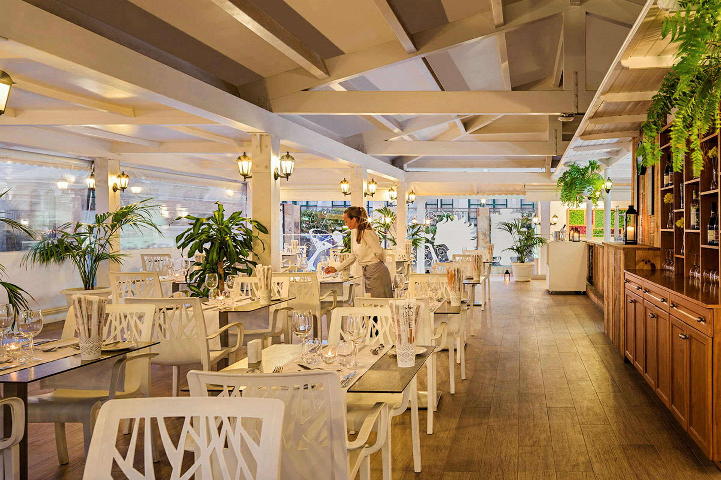 Interiør af en restaurant med træelementer, hvide møbler og grønne planter. (AI-genereret tekst)