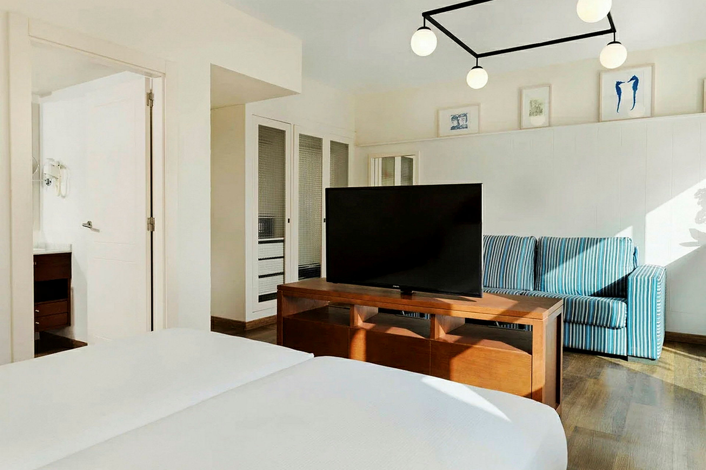 Et hotelværelse med en dobbeltseng, et fjernsyn på et træbord, en blåstribet sofa og vægdekorationer. (AI-genereret tekst)