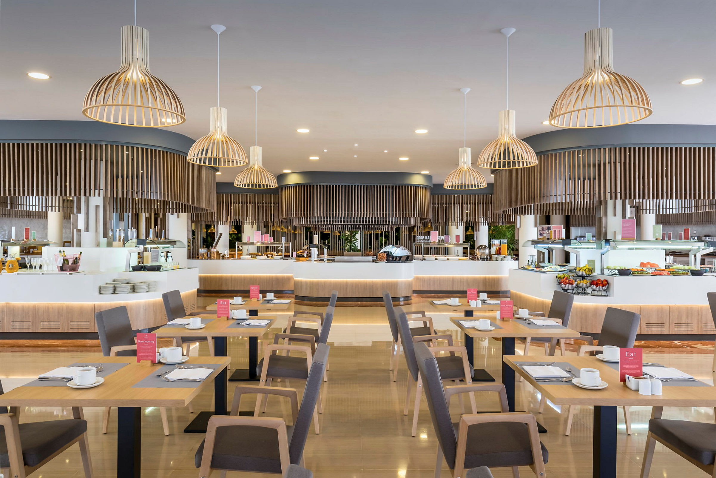 En restaurant med træborde og stole, serveringsområde i baggrunden med lamper hængende fra loftet. (AI-genereret tekst)