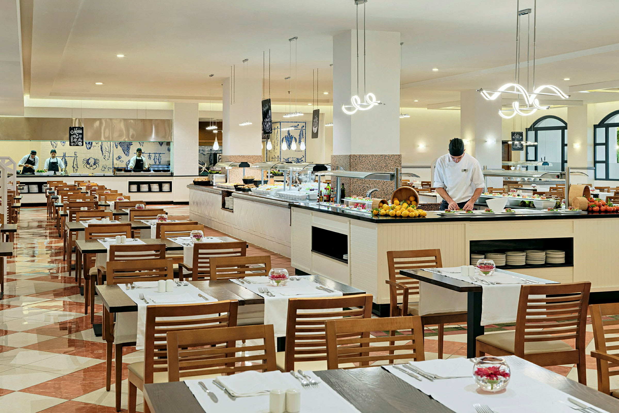 Restaurant med dækkede borde og en buffet. Personale arbejder ved madstationen. (AI-genereret tekst)