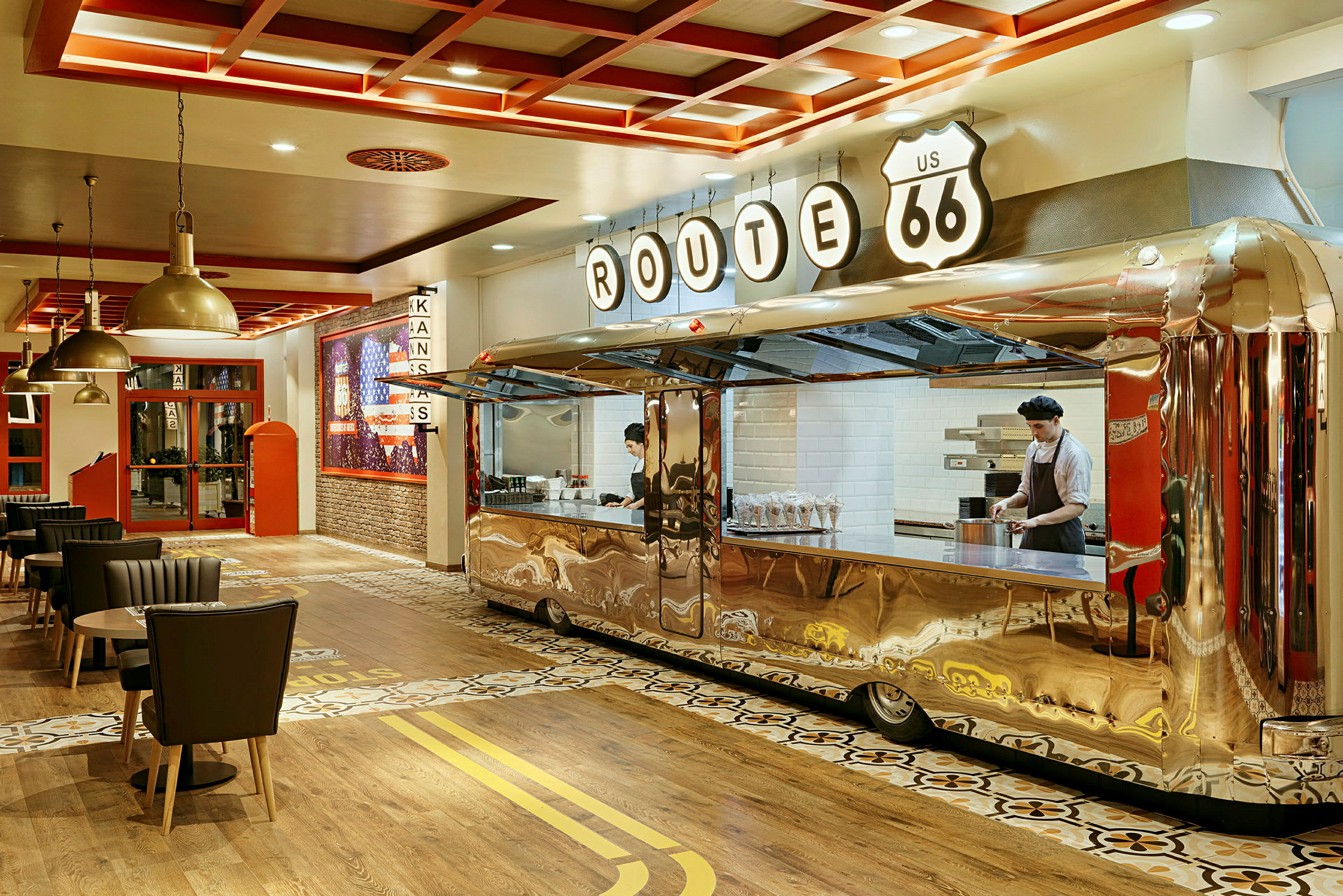 Et interiør af en restaurant med et retrotema, hvor en serveringsdisk er designet som en skinnende trailer, og flere spiseborde og stole er placeret rundt omkring. (AI-genereret tekst)