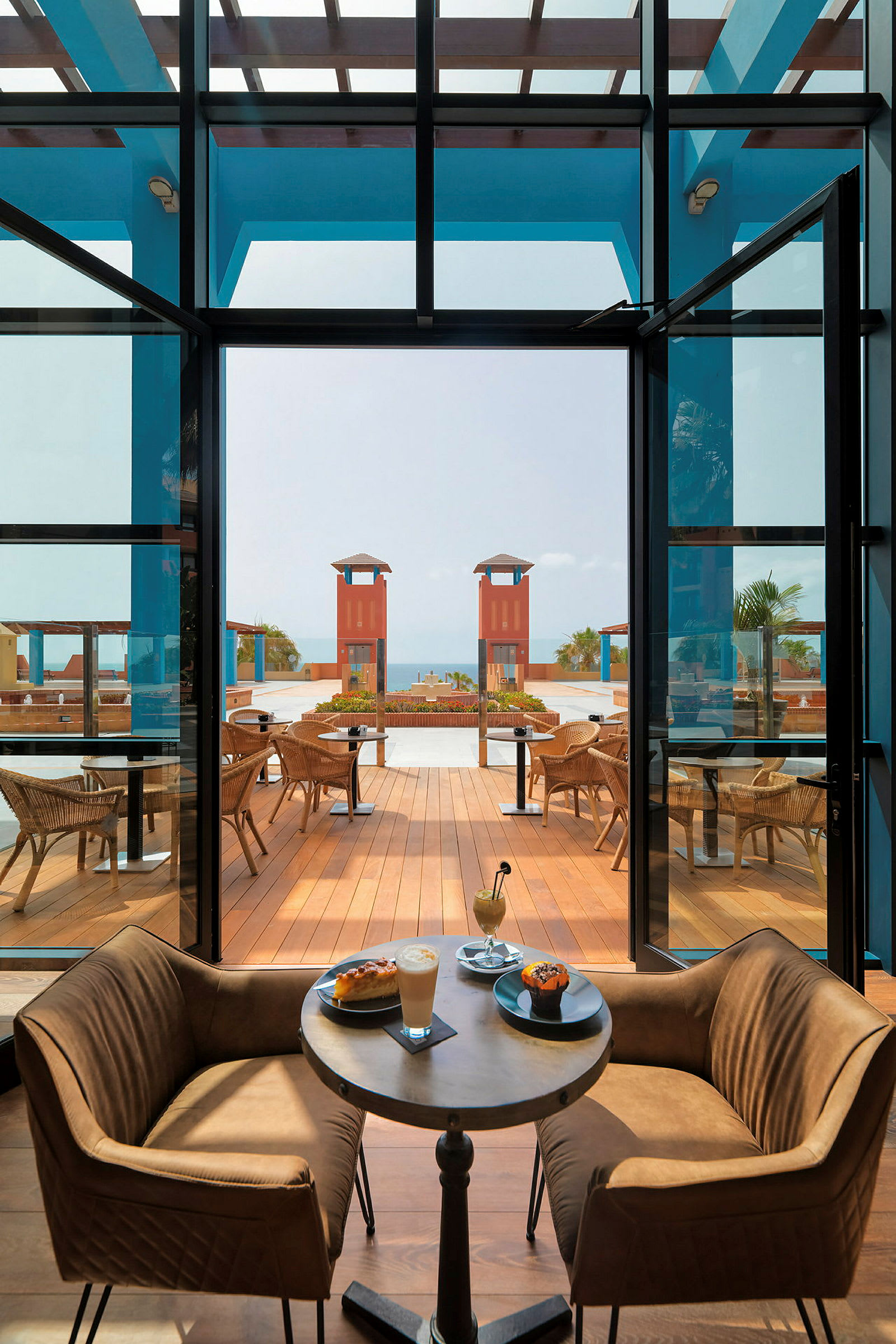 Interiør af en restaurant med borde og stole, med smuk udsigt over en terrasse og havet. (AI-genereret tekst)