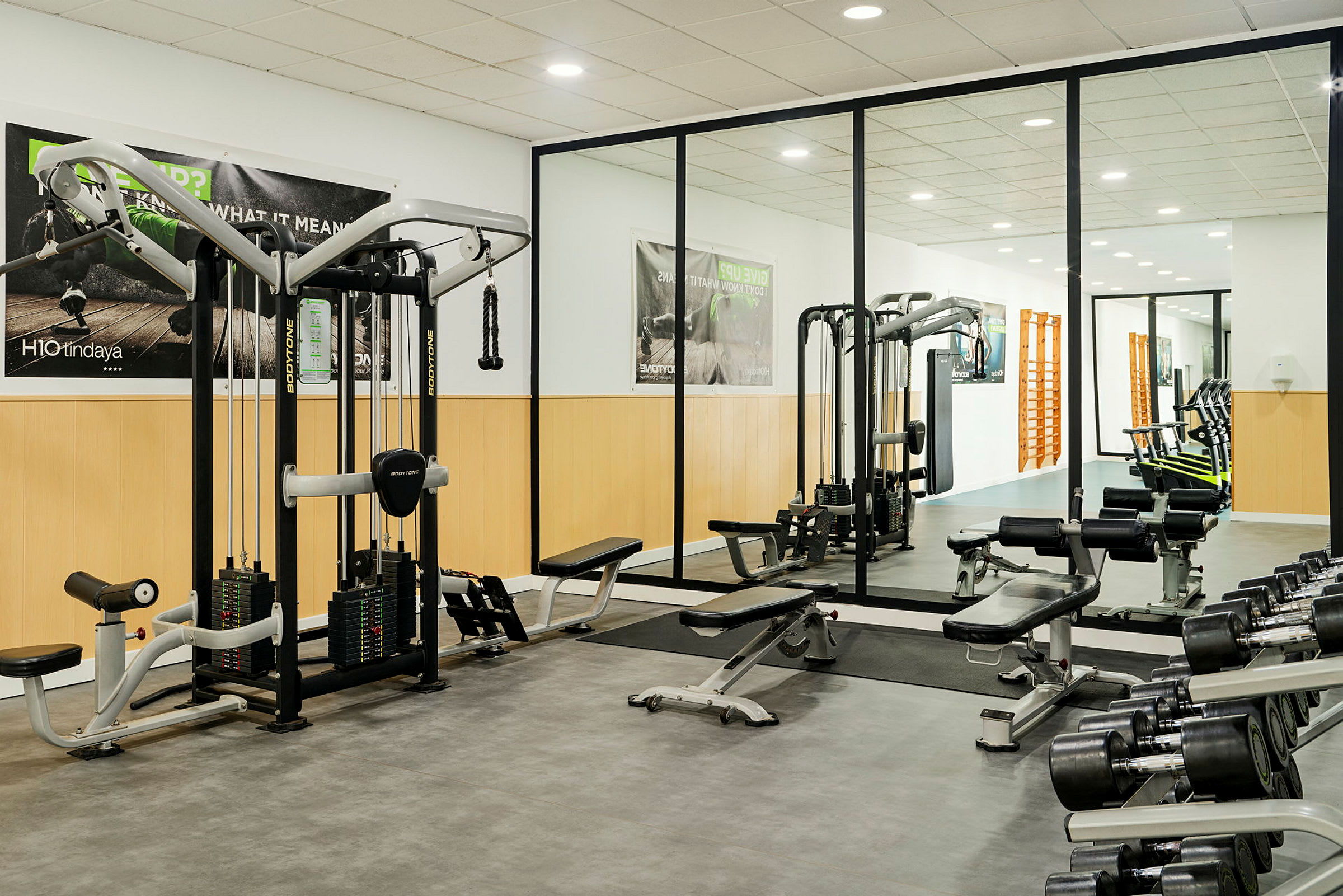 Et fitnesscenter med træningsudstyr, inklusive vægte, træningsbænke og kabelmaskiner. Spejlvægge ses i baggrunden. (AI-genereret tekst)