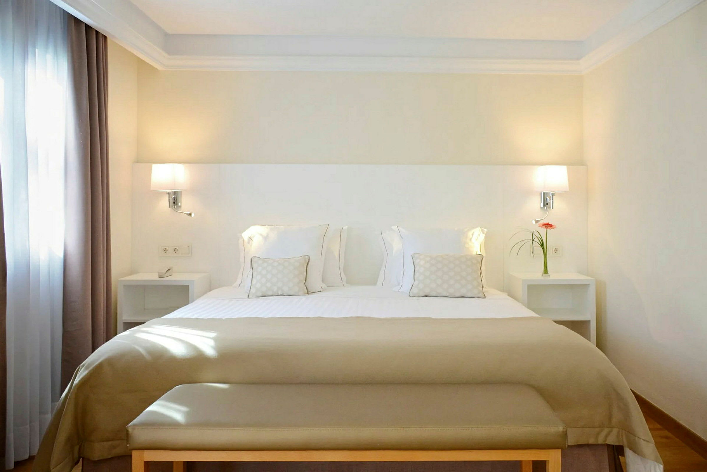 Et hotelværelse med en bred seng dekoreret med hvidt og beige sengetøj samt natborde med lamper og dekorationer. (AI-genereret tekst)