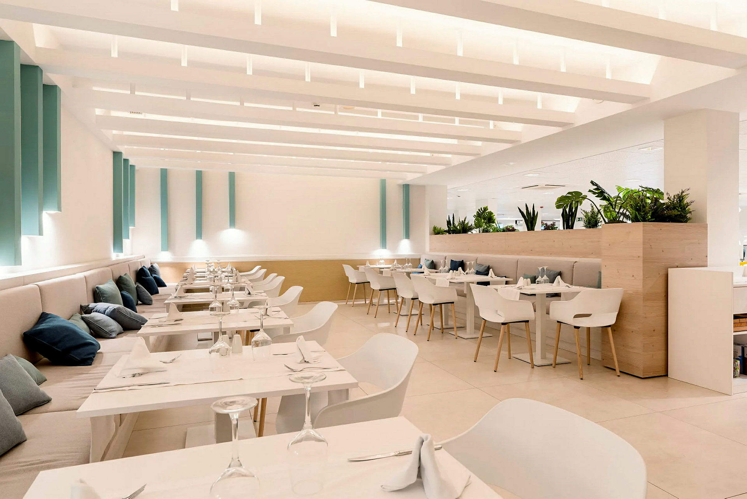 Et lyst og moderne indrettet restaurantområde med hvide møbler og grønne planter. (AI-genereret tekst)