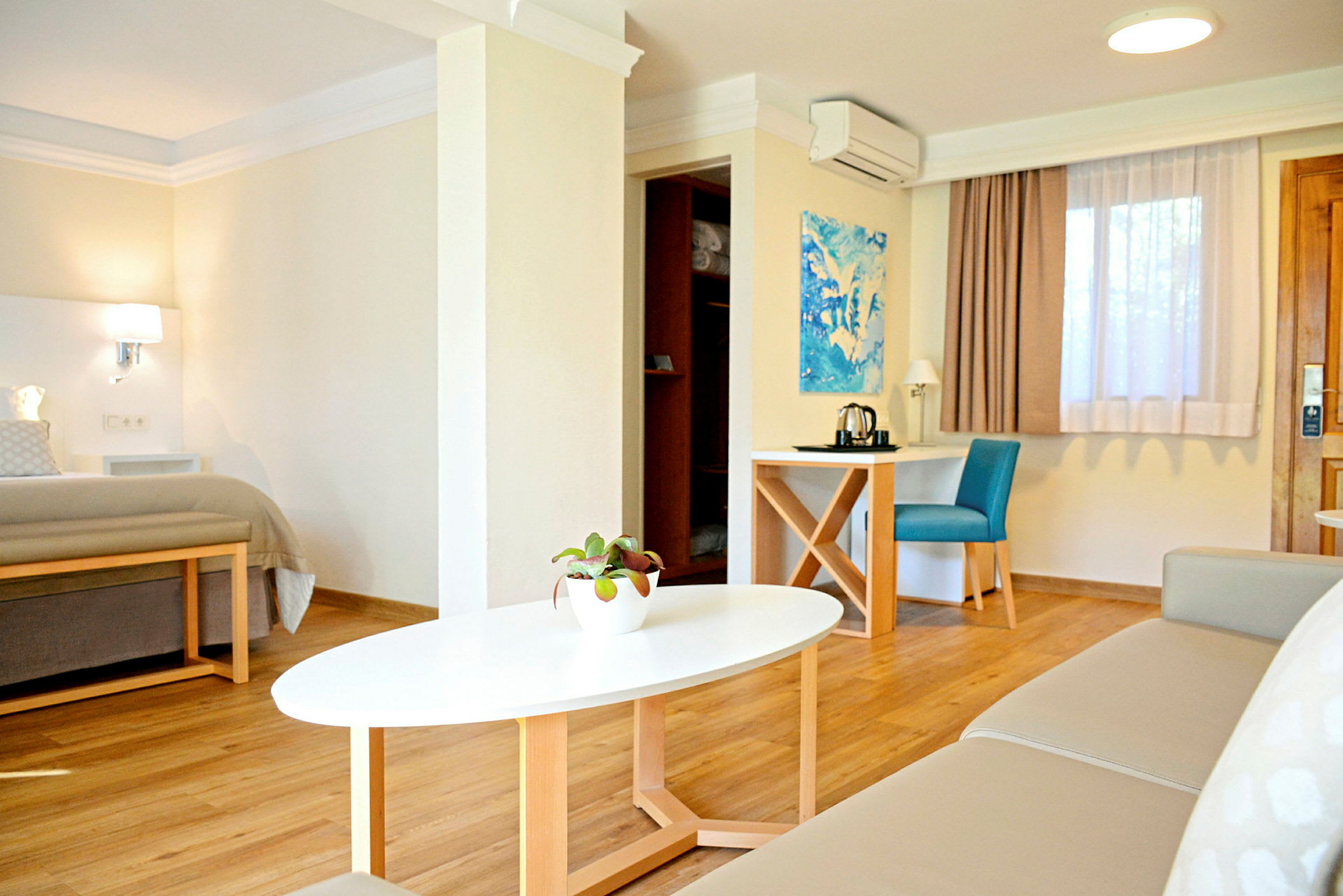 Et moderne og lyst hotelværelse med en seng, en sofa, et sofabord og et skrivebord med en stol. (AI-genereret tekst)
