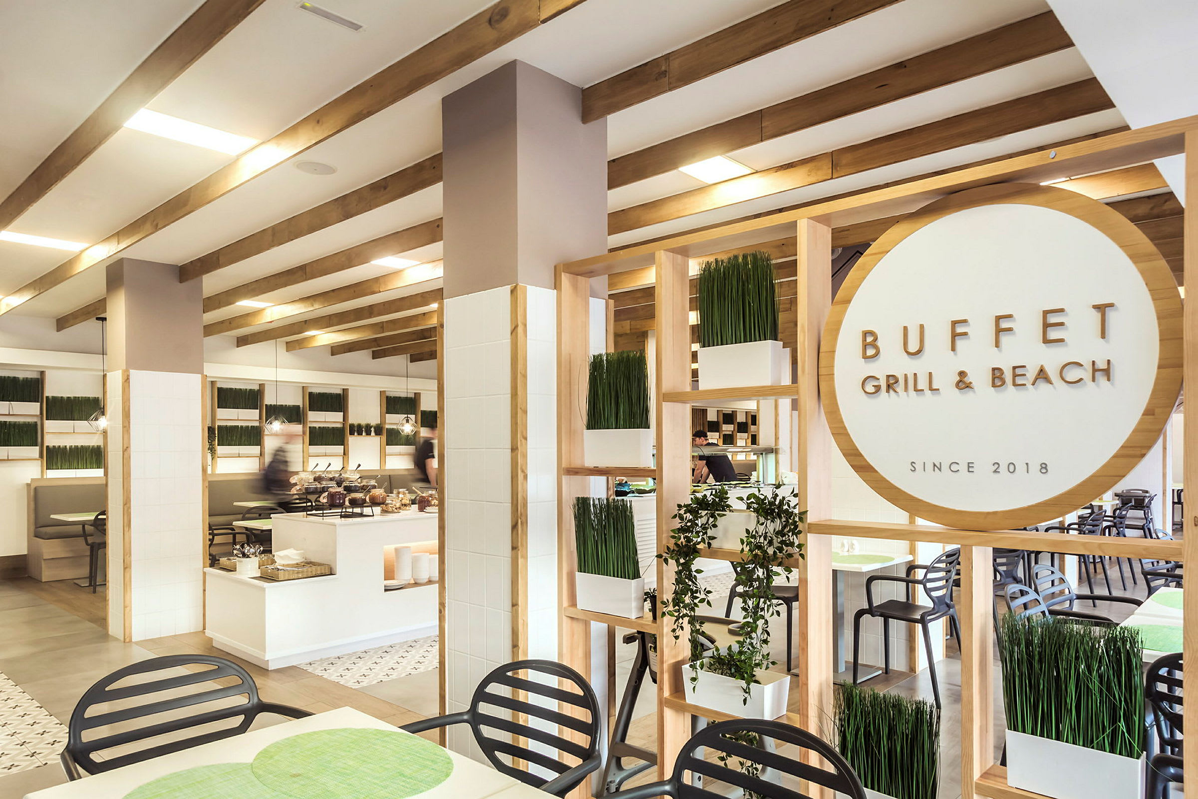 Interiør af en restaurant med buffet, med træpaneler, plantepynt og et skilt med teksten "Buffet Grill & Beach". (AI-genereret tekst)