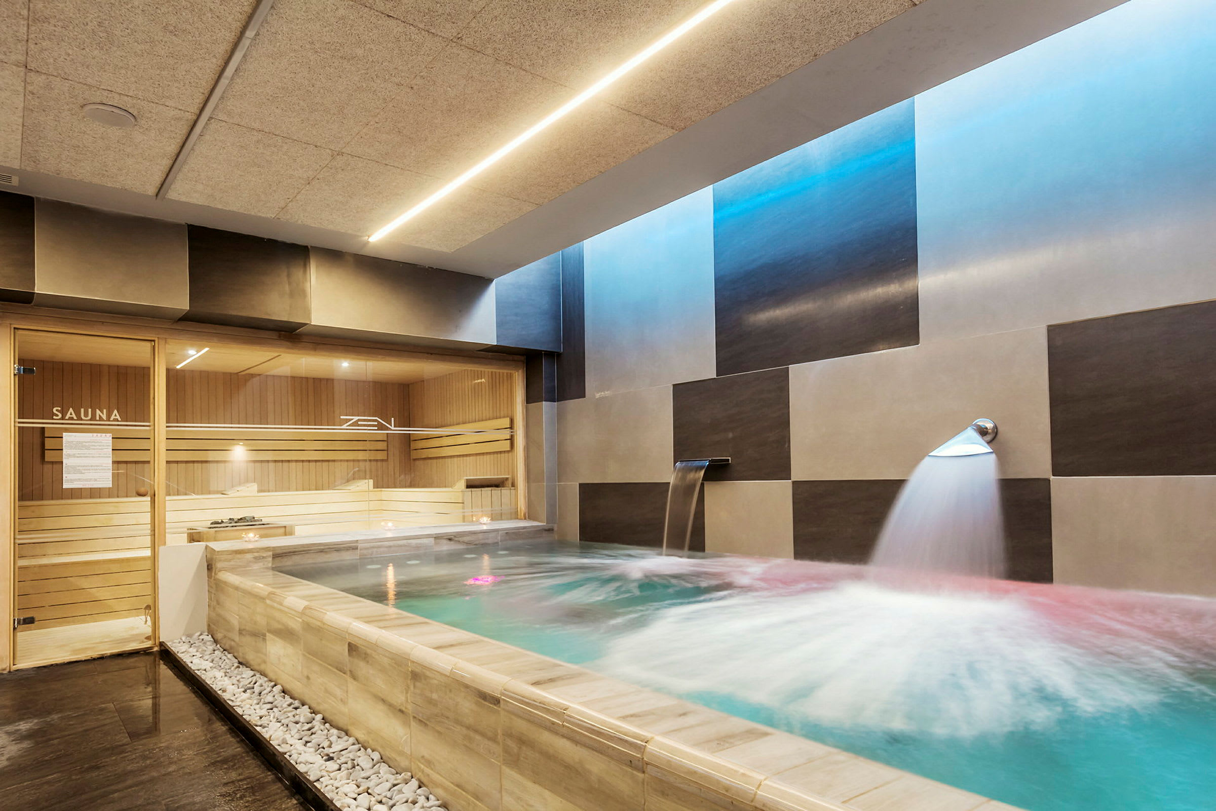 Et indendørs pool med fontæne og moderne indretning ved siden af en sauna. (AI-genereret tekst)